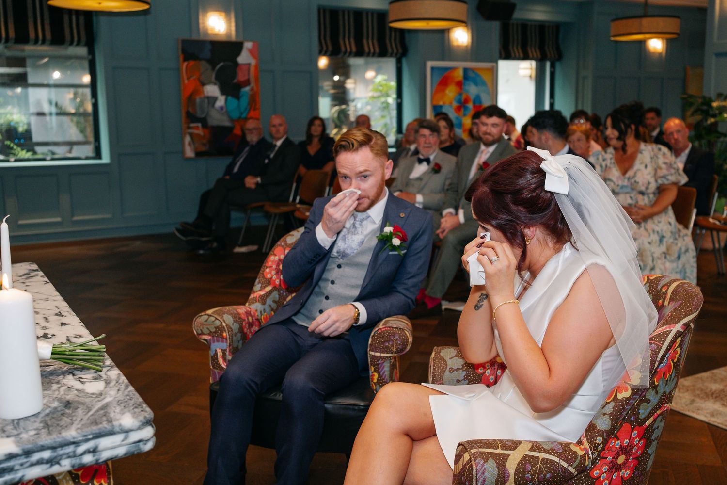 Emotional wedding ceremony moment captured in a modern venue with teal walls and pendant lighting.