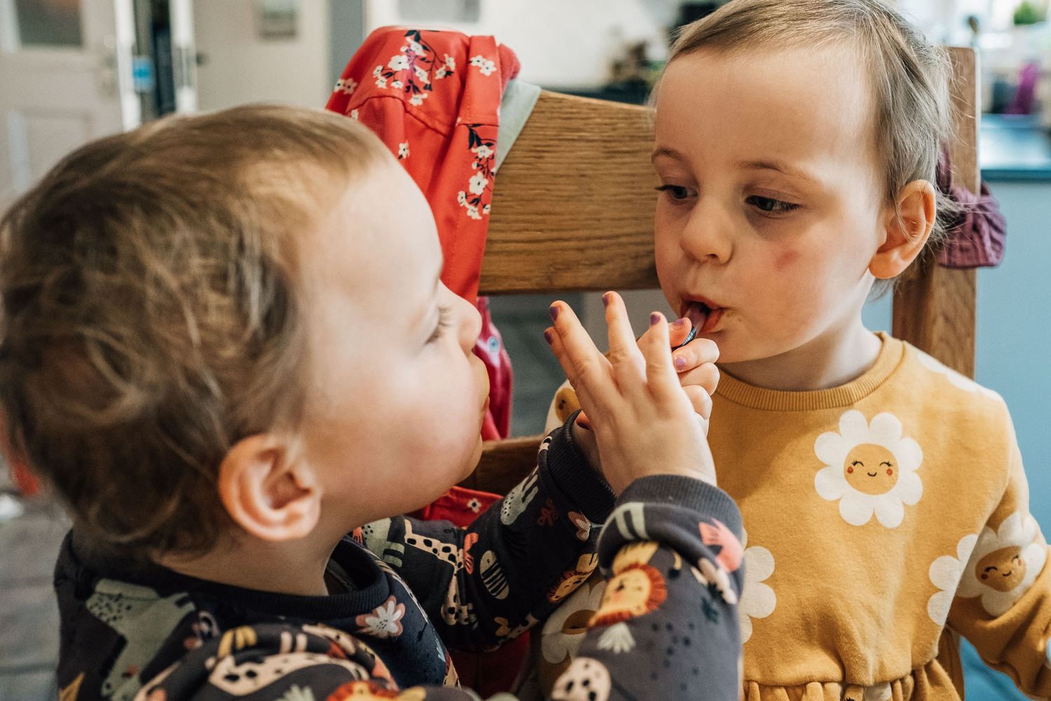 Two children share a close moment while seated at wooden furniture.