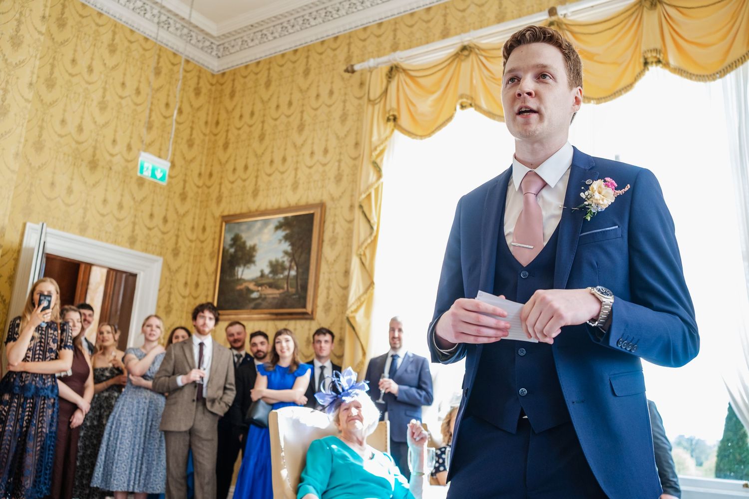 Guests socialize and enjoy a celebration in an elegant yellow drawing room with ornate moldings and decor.