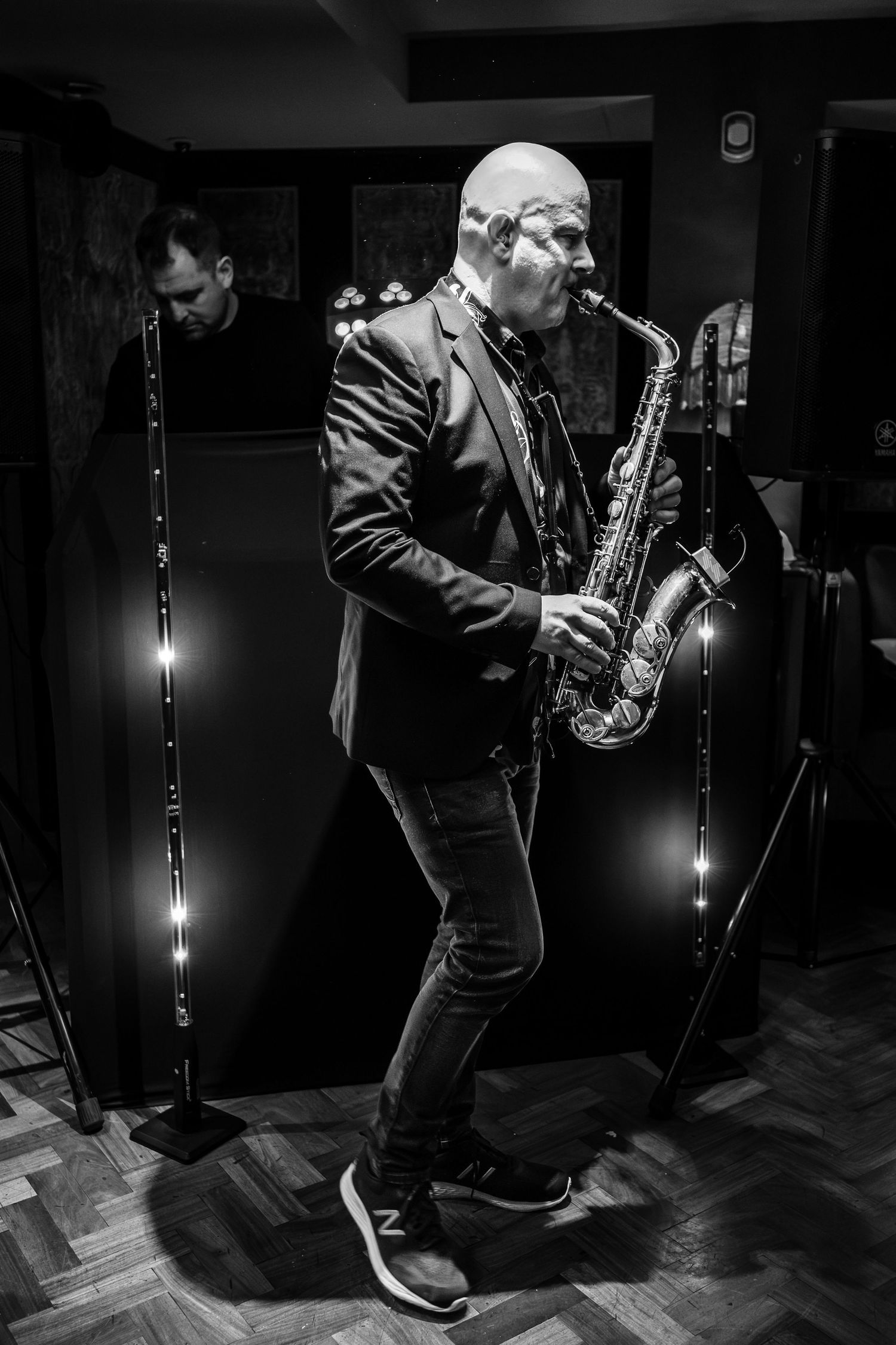 A saxophone player performs on stage in black and white dramatic lighting.