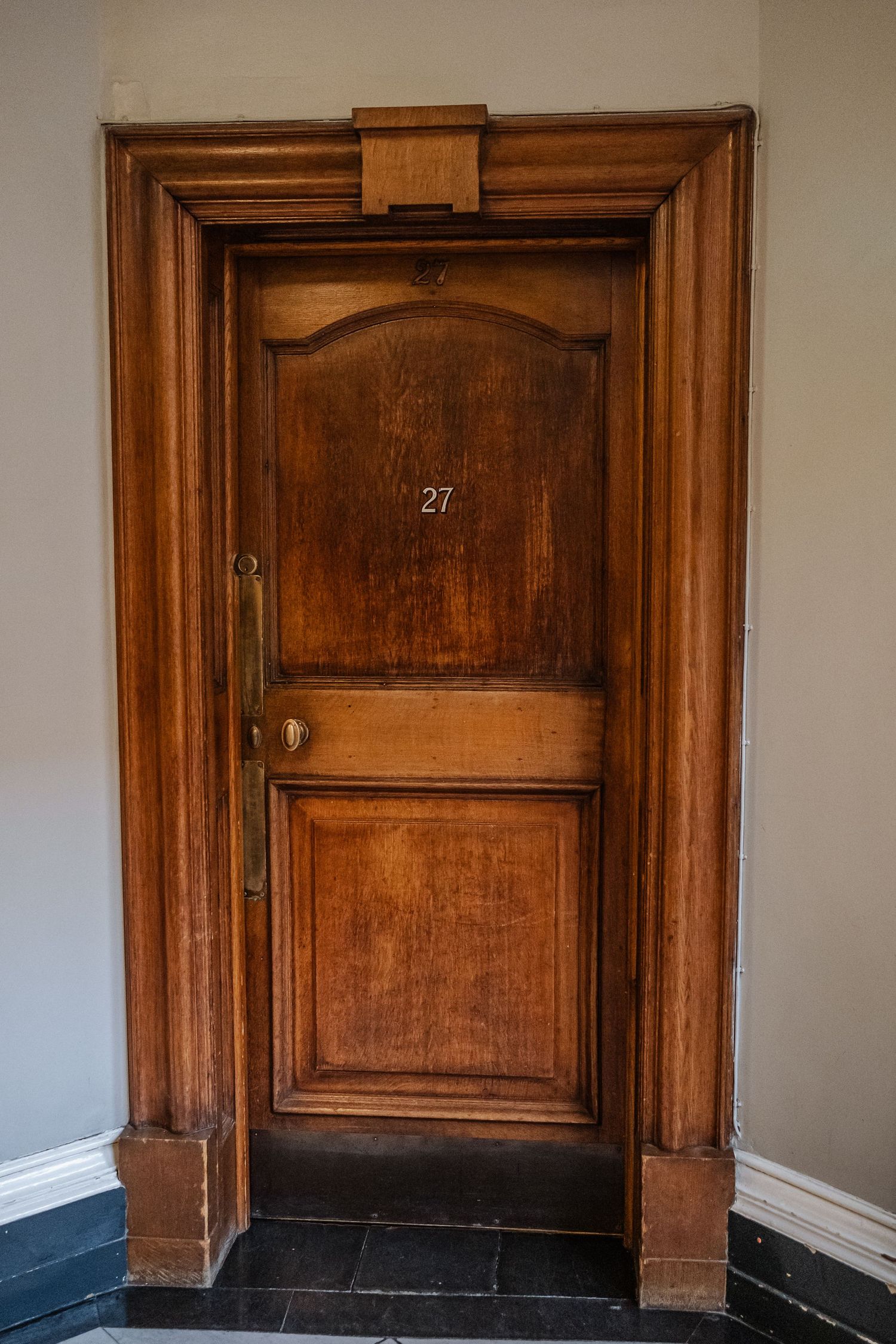 Vintage wooden door numbered 27 with ornate molding and dark stained finish in a hallway.