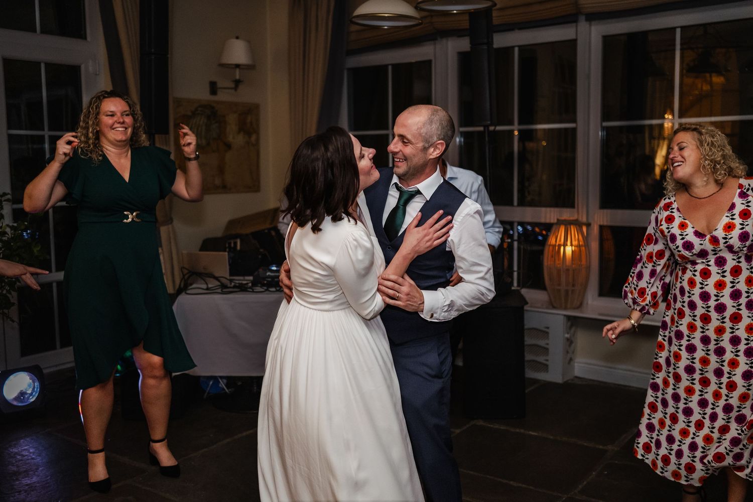 Bride and groom share a joyful first dance surrounded by smiling wedding guests in an elegant reception venue.