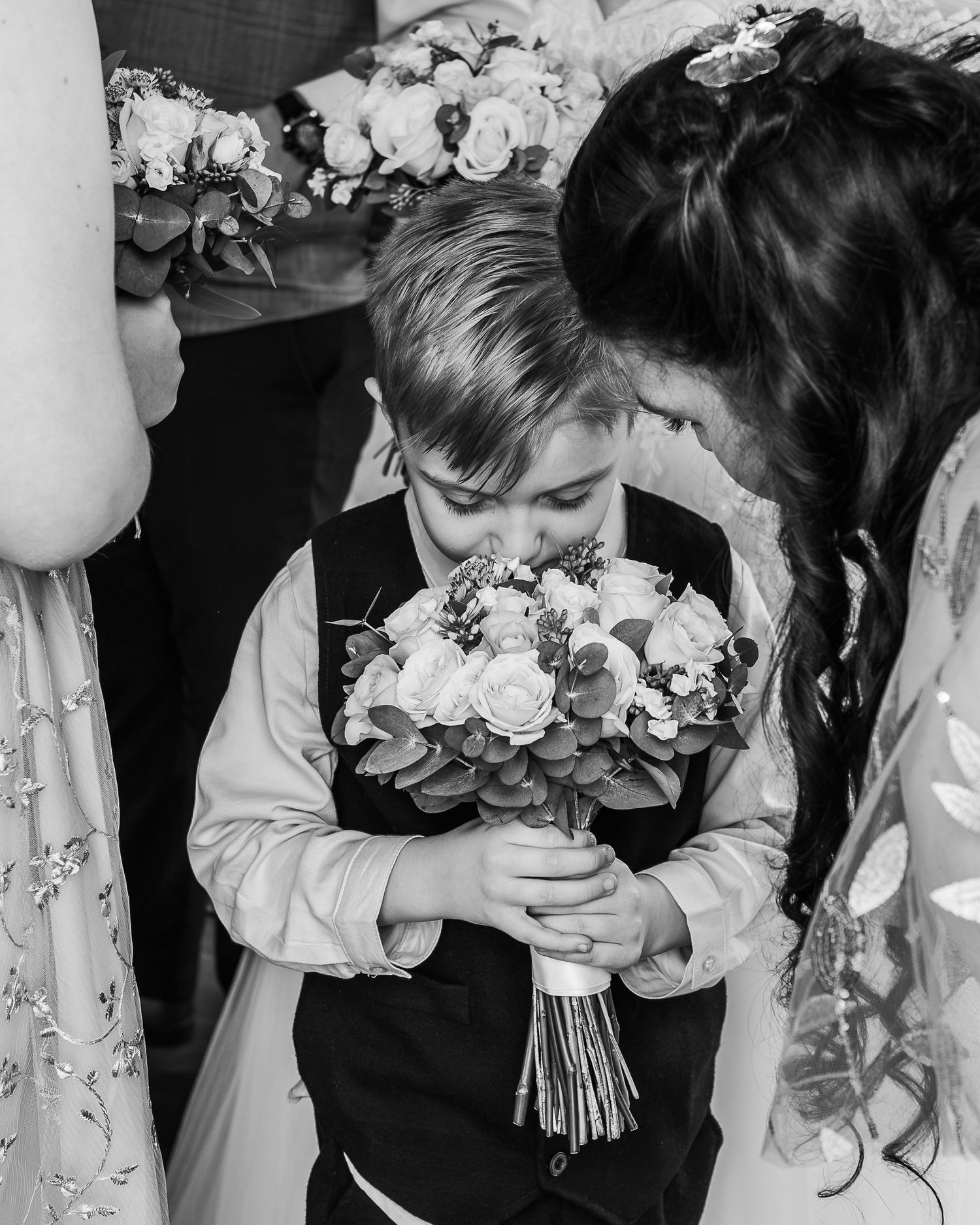 A black and white capture shows a small child in formal wear carefully holding a wedding bouquet.