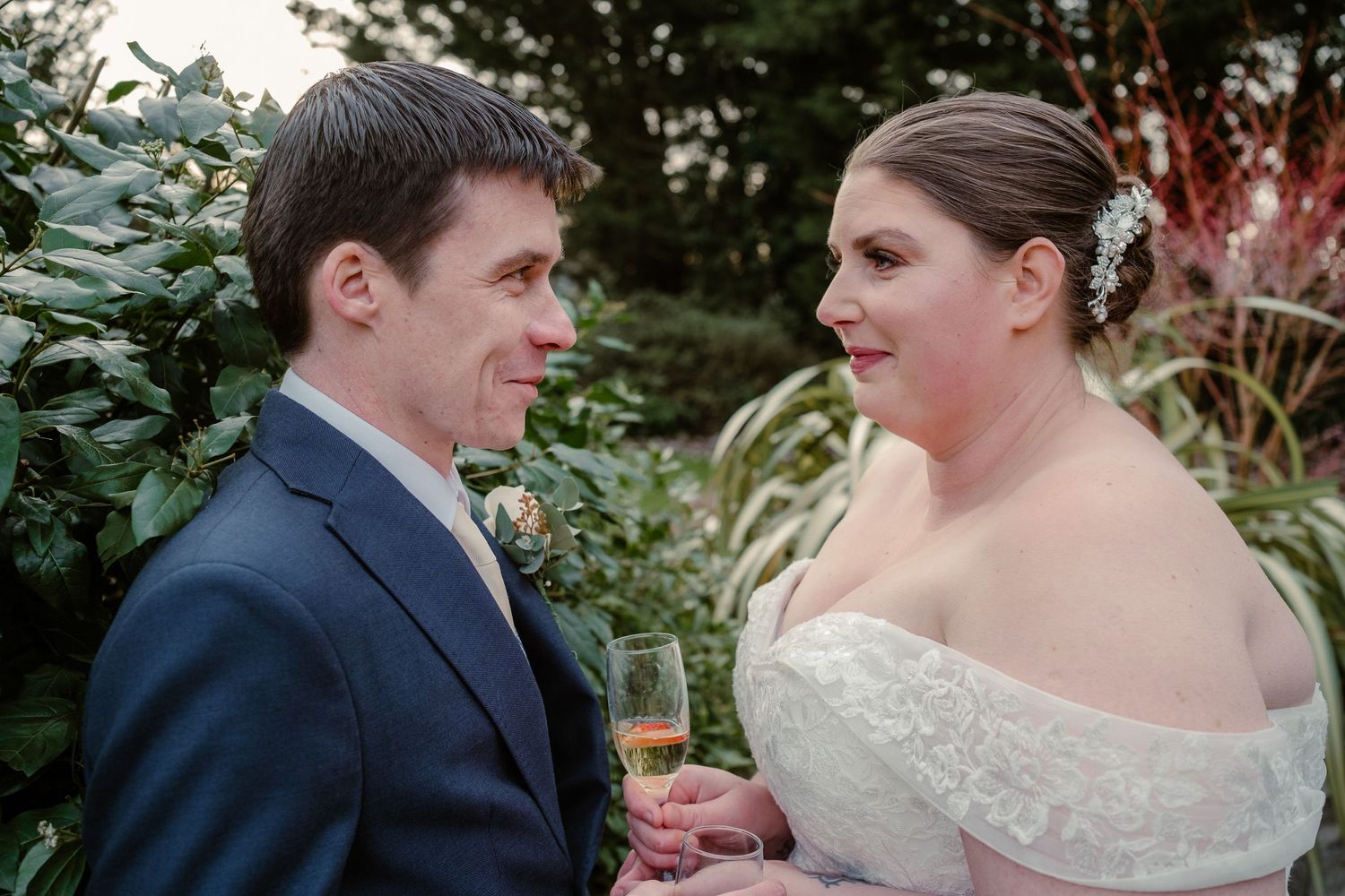 Wedding couple sharing champagne in a garden setting during golden hour.