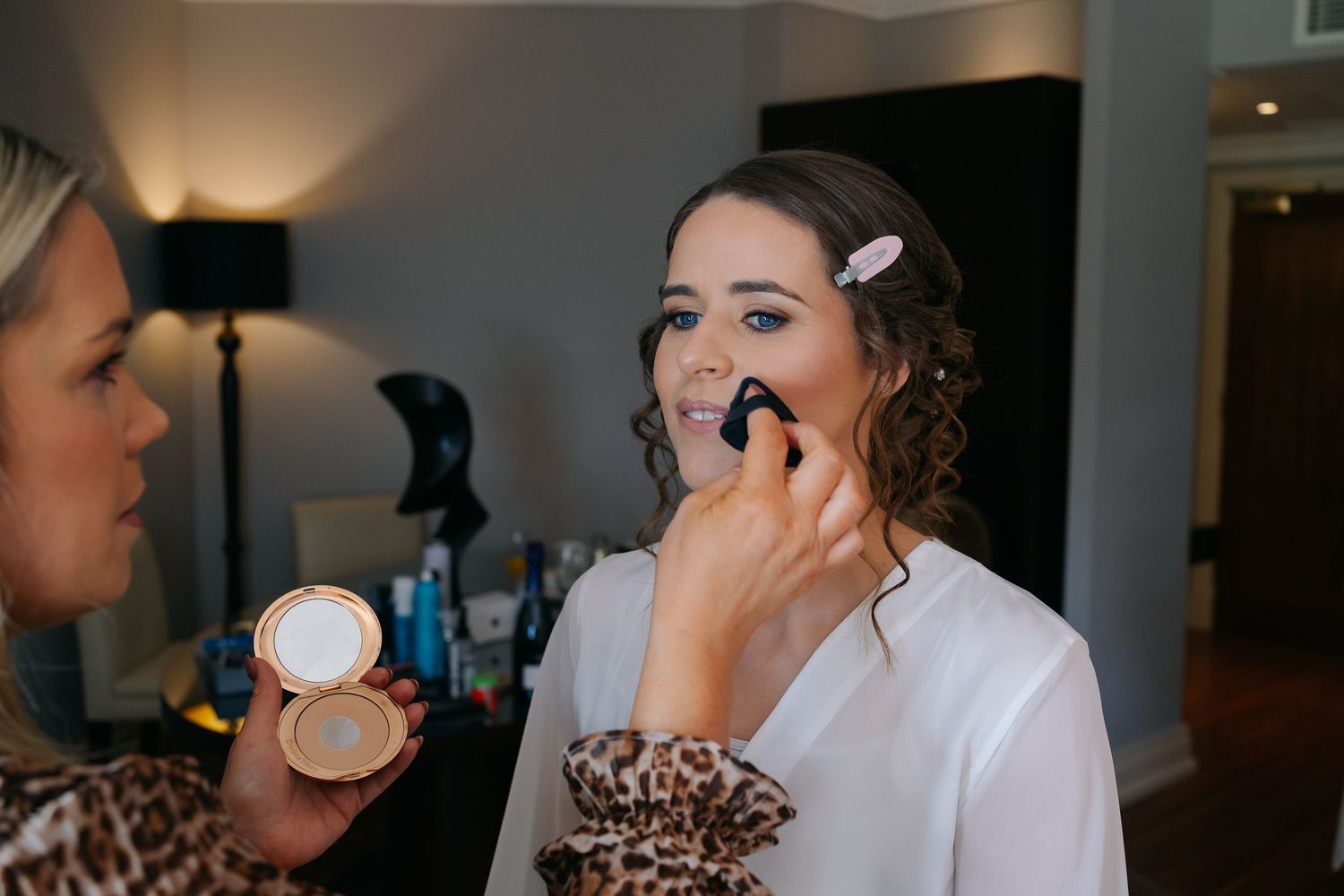 Professional makeup artist applying cosmetics on a client wearing a white robe during a beauty preparation session.