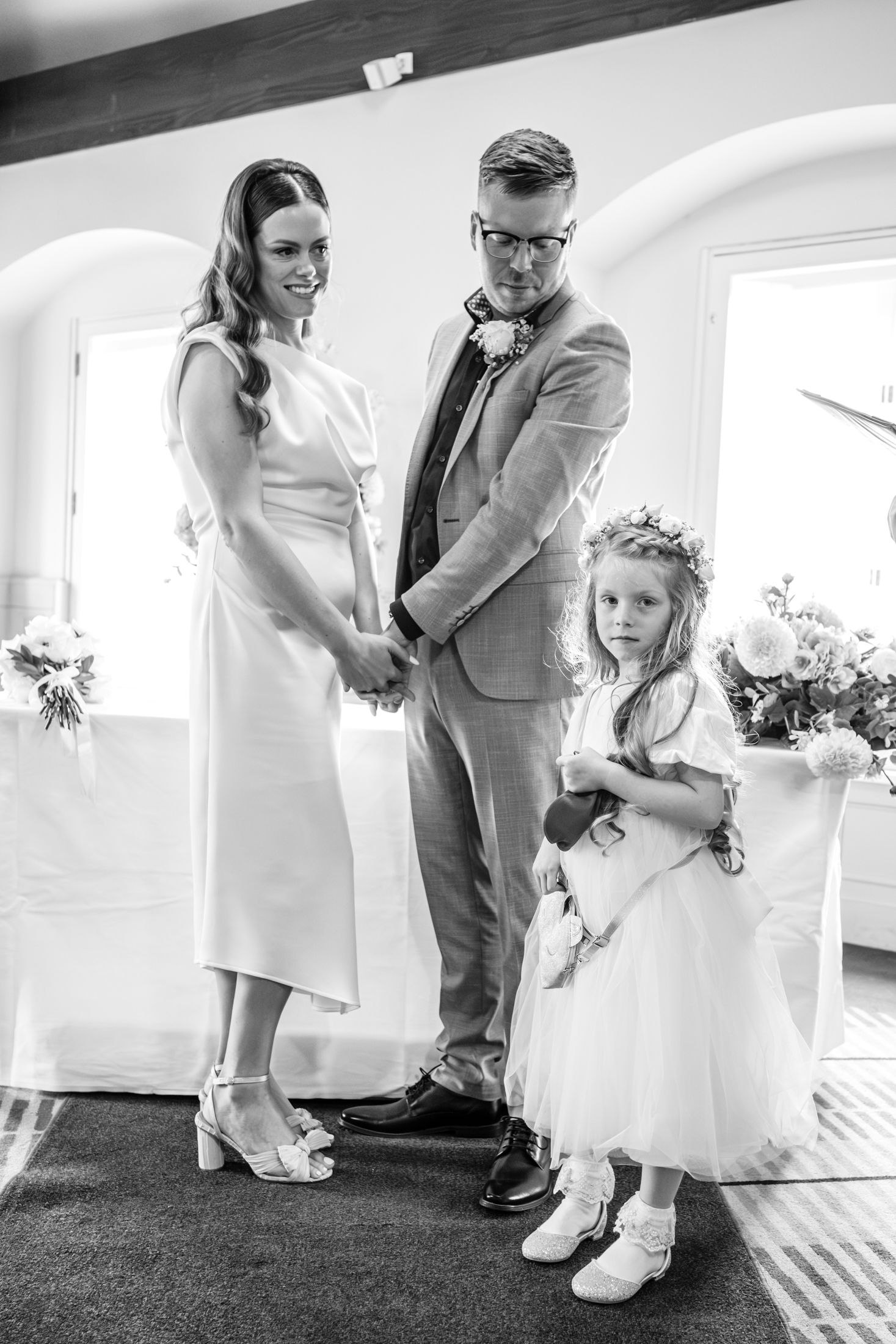Three wedding attendees stand together during a black and white ceremony moment in an elegant venue.