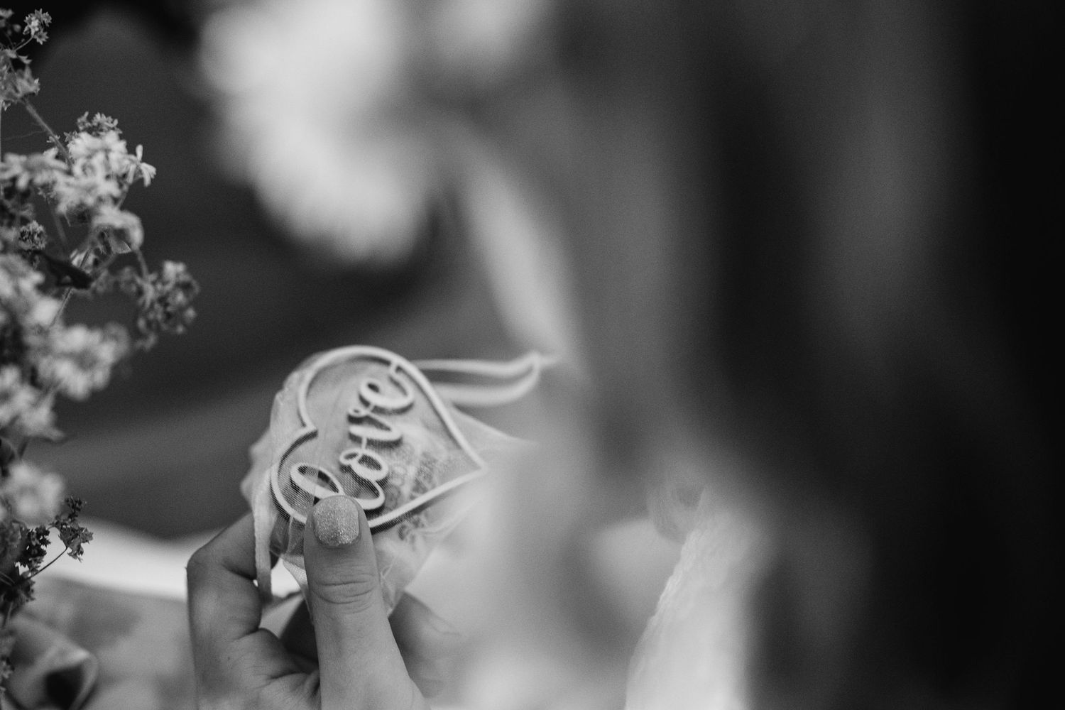 Black and white photo of hands holding a heart-shaped token with the word Love engraved on it.