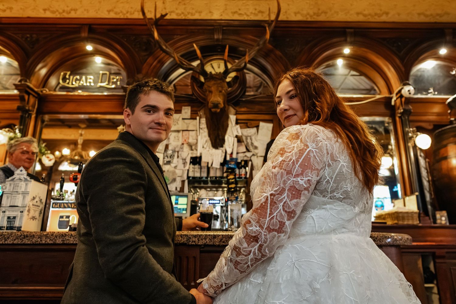 A couple posing in front of a traditional Irish pub bar with mounted deer head.