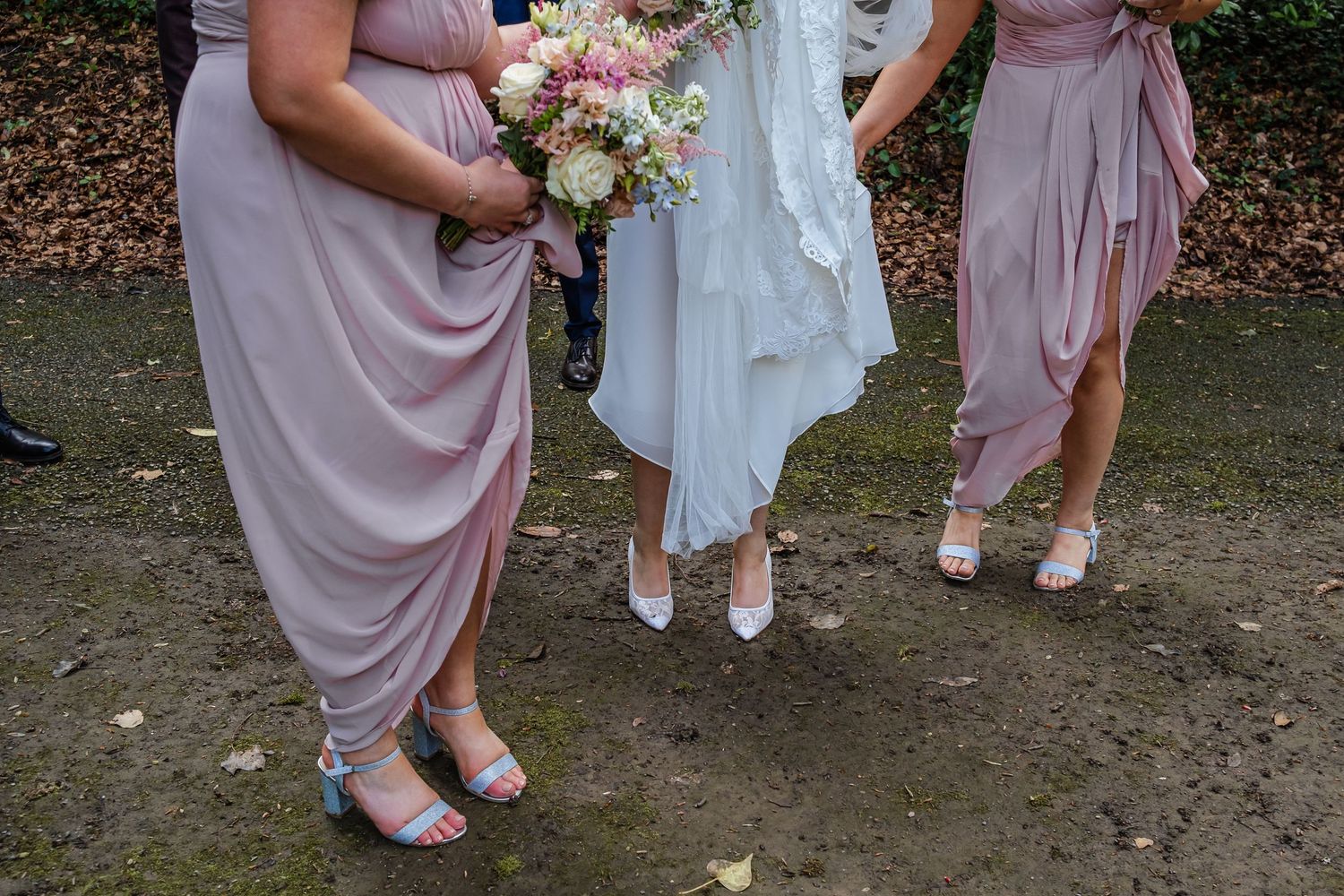 Wedding party members showcase elegant dusty rose dresses and floral bouquets in an outdoor garden setting.