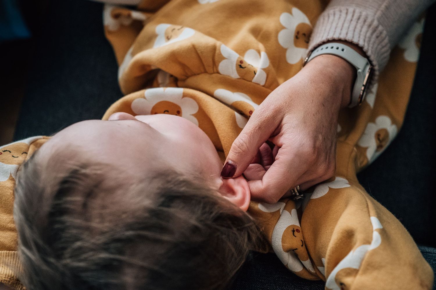 Close-up of a hand touching while resting on a yellow patterned blanket.
