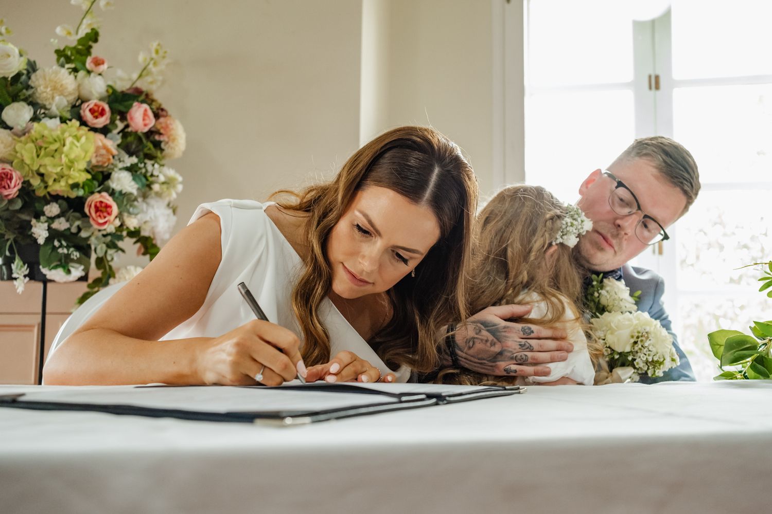 Wedding ceremony participants sign official documents at a decorated table.