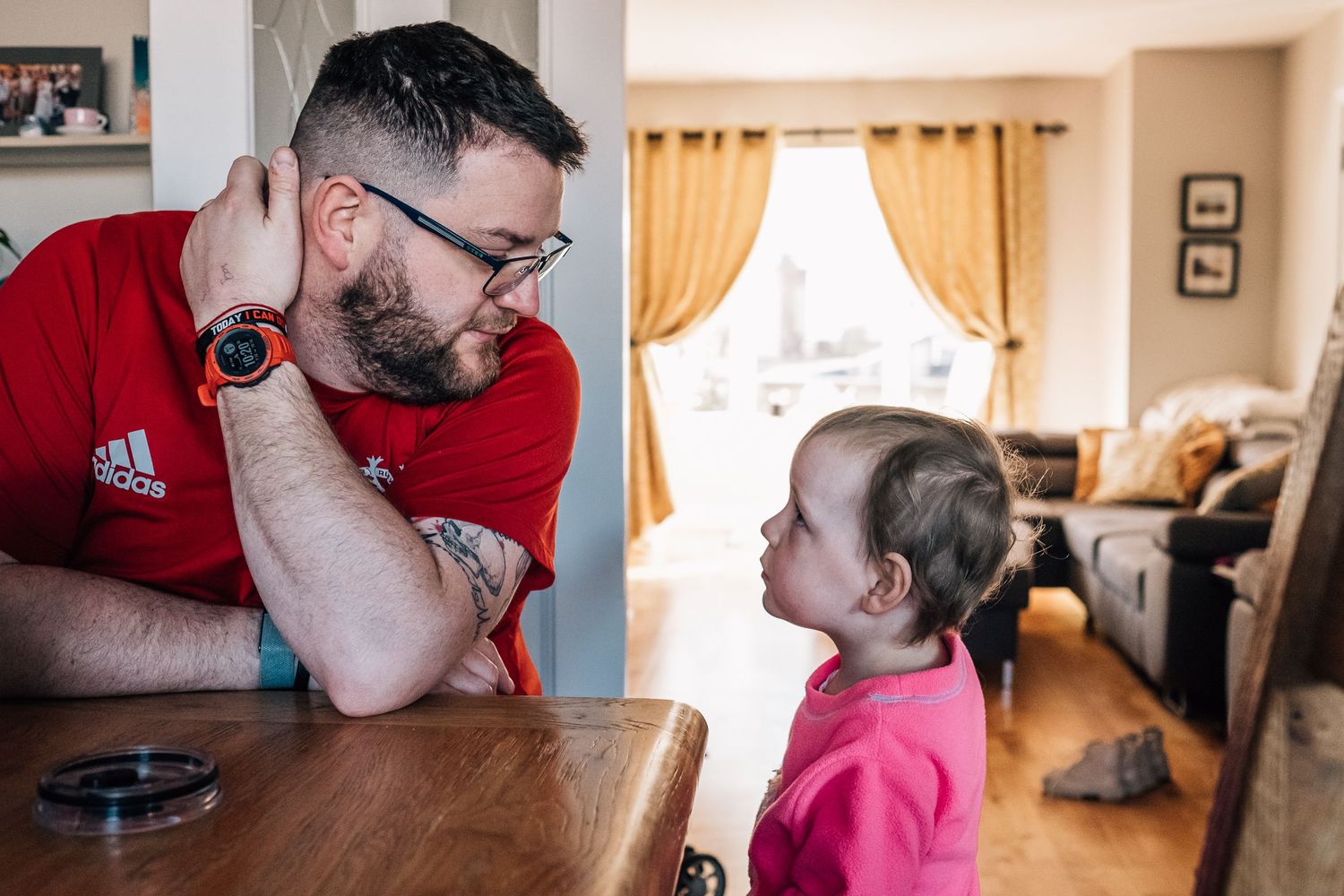 An intimate conversation moment captured across a wooden table in a cozy living room setting.
