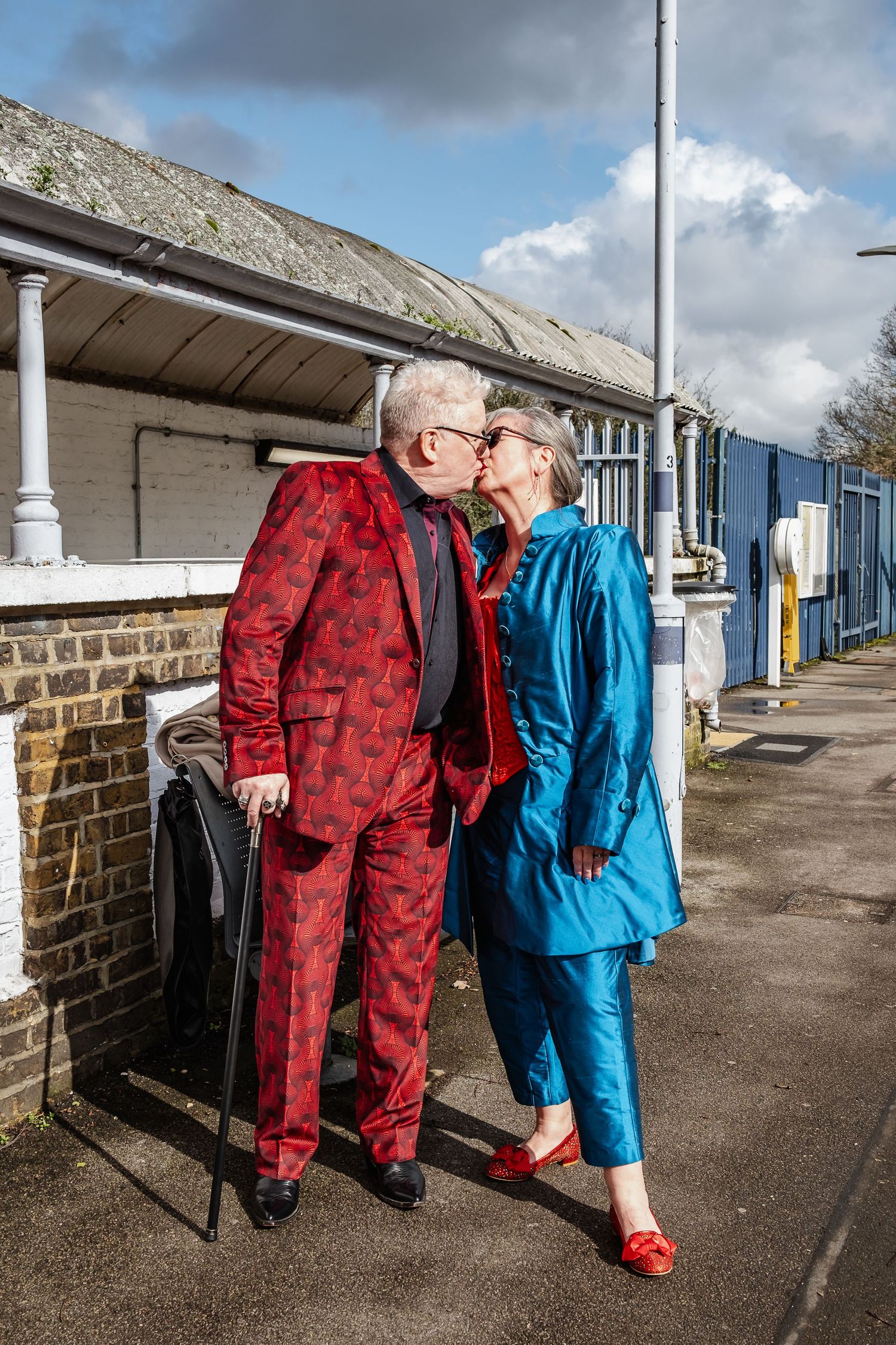 A couple in vibrant red and blue outfits standing together on a platform.