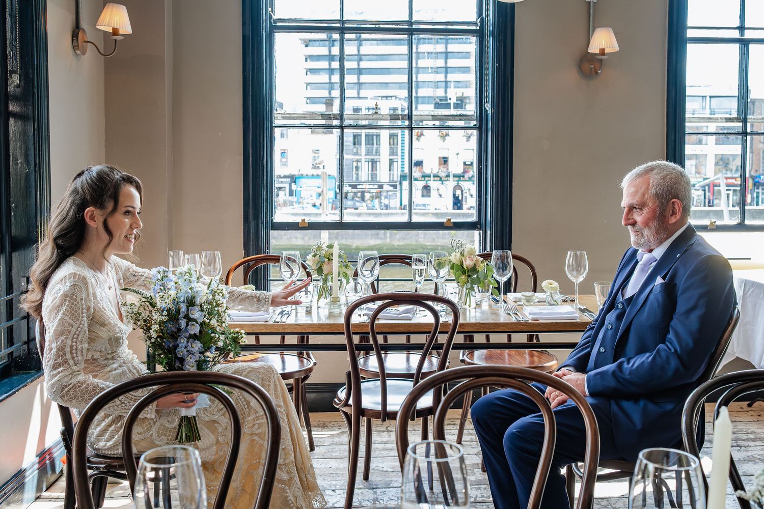 Elegant wedding reception venue with large windows, natural light, and white table settings.