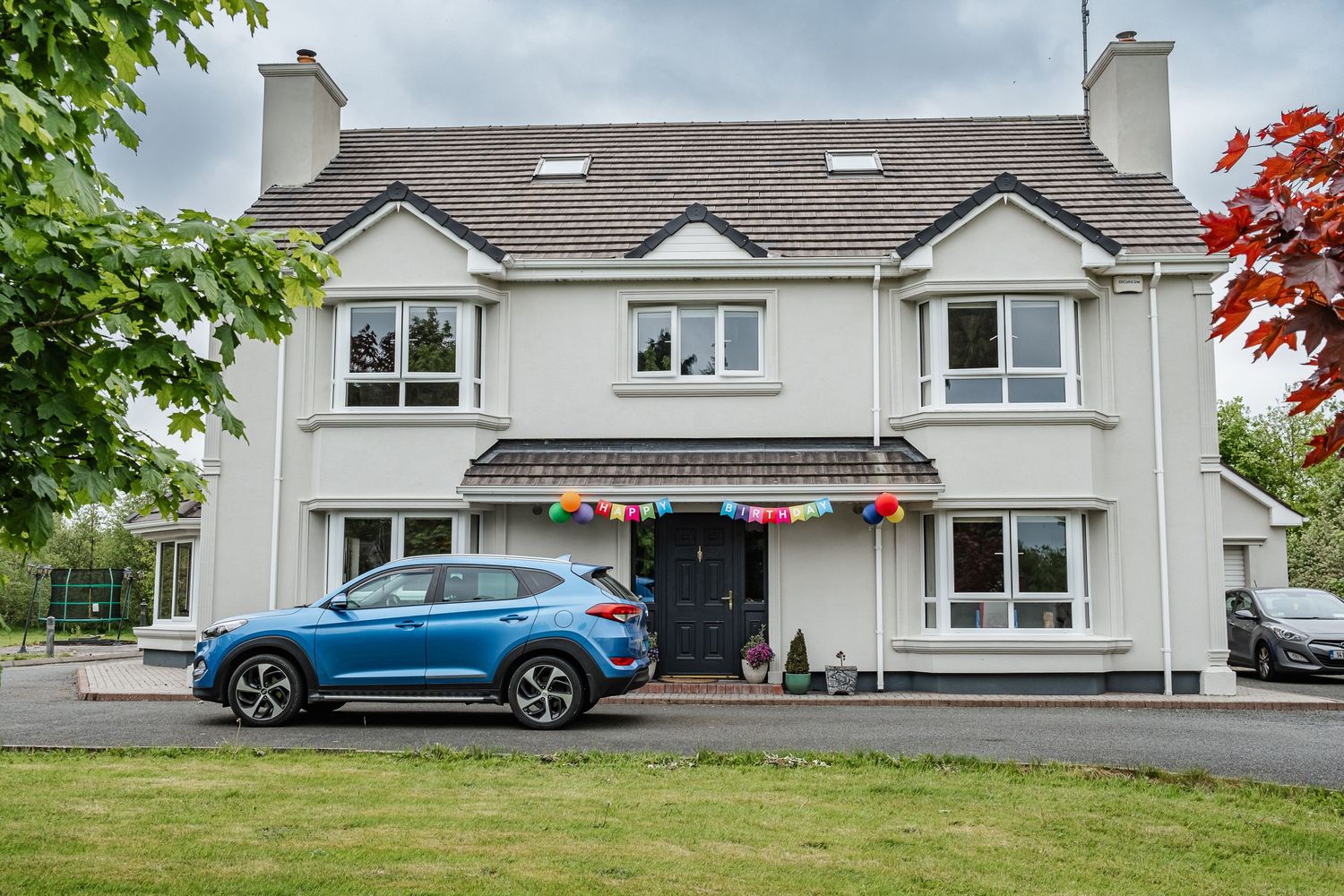 Modern white house with blue car parked in front and festive bunting decorating the entrance.