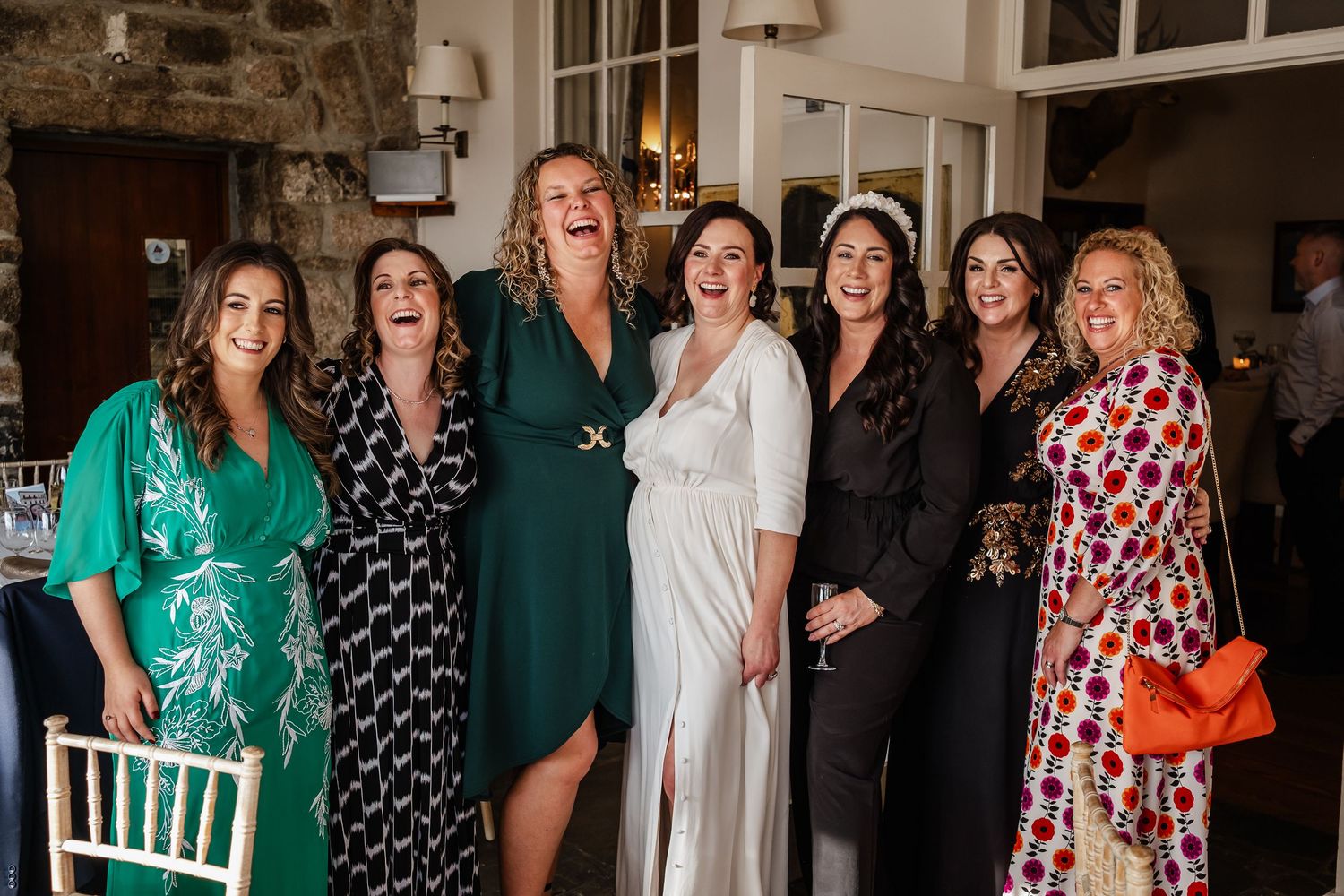 Group of six women posing and laughing together at a wedding celebration.