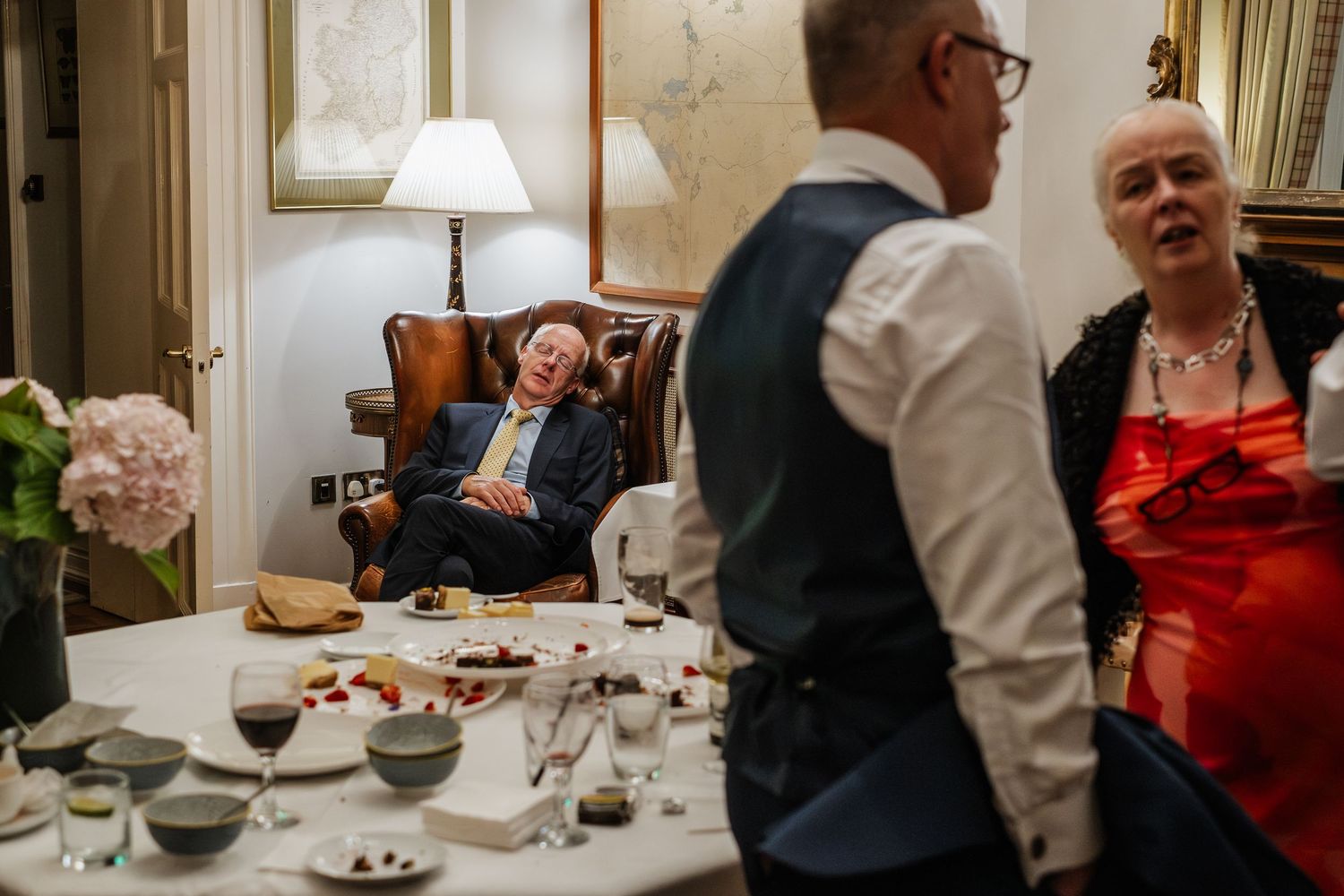 Elderly wedding guest relaxing in armchair laughing during wedding reception gathering.