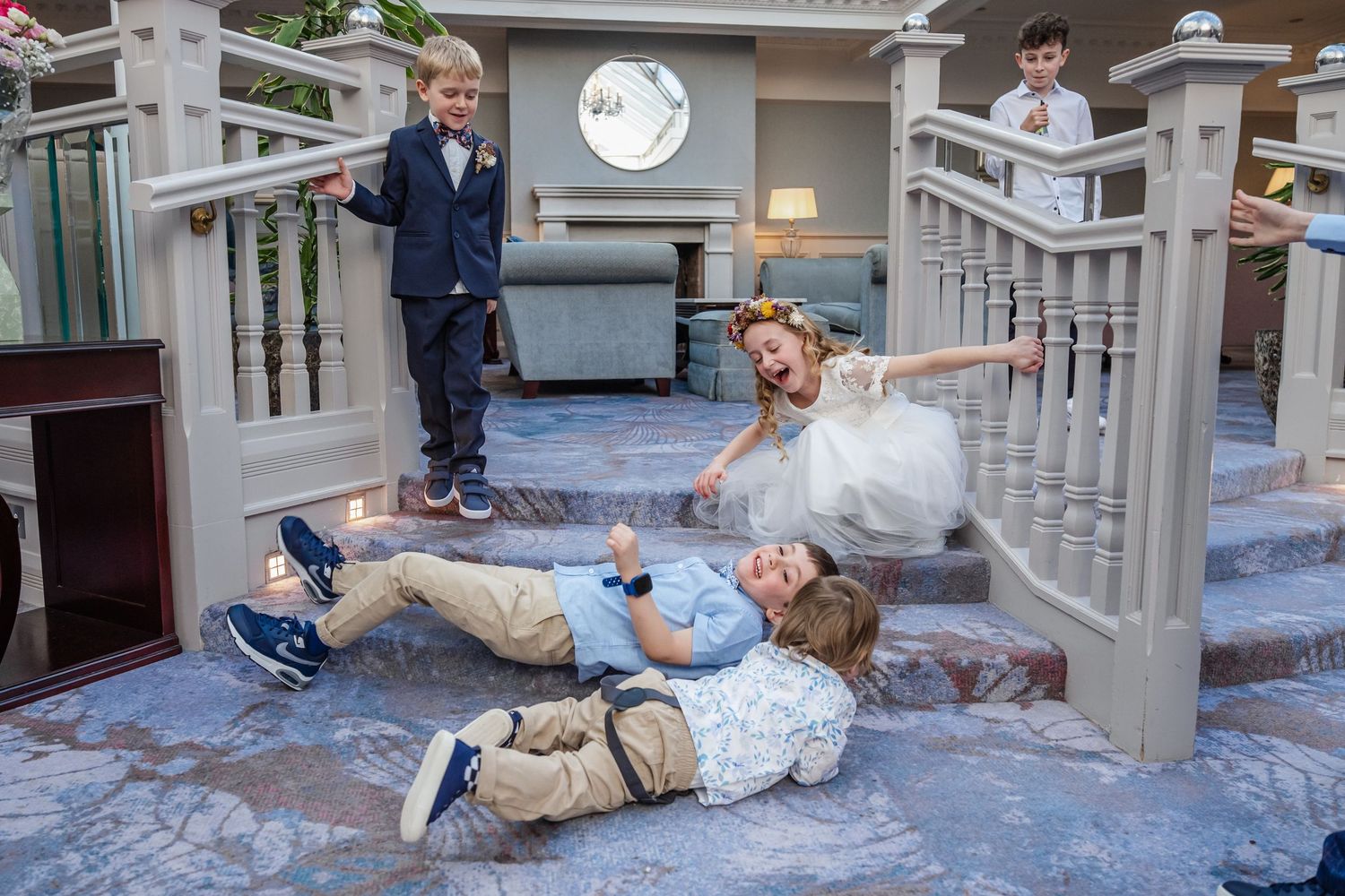 Children playing on decorative stairs at a wedding, with boys in suits and a girl in a white flower girl dress.