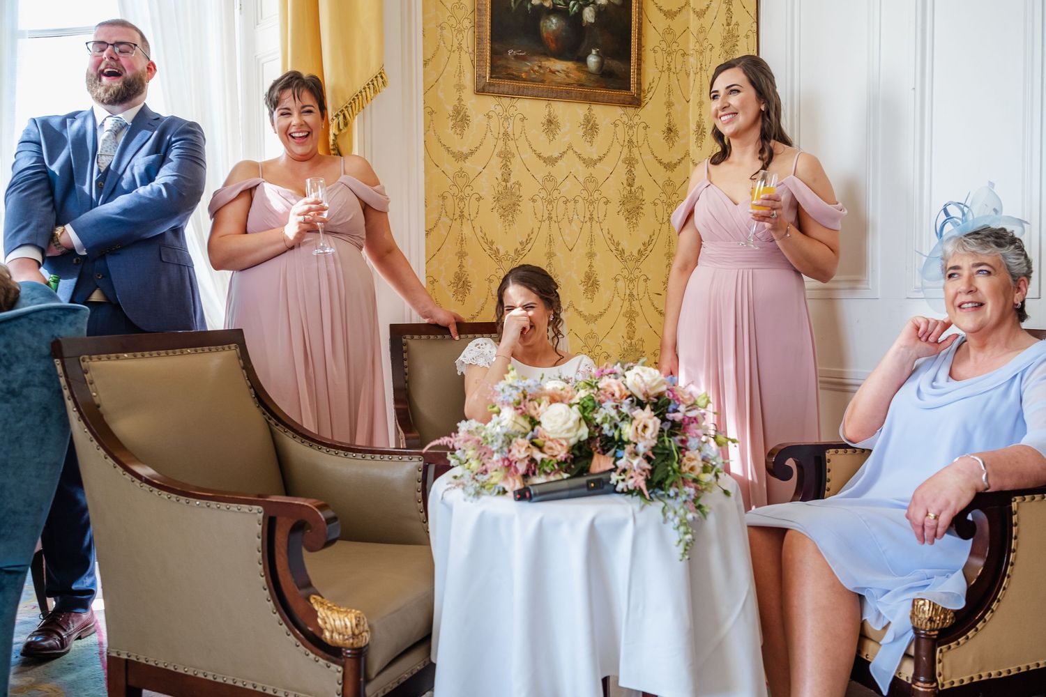 People share joyful reactions while getting ready in an elegant room decorated with ornate golden wallpaper.