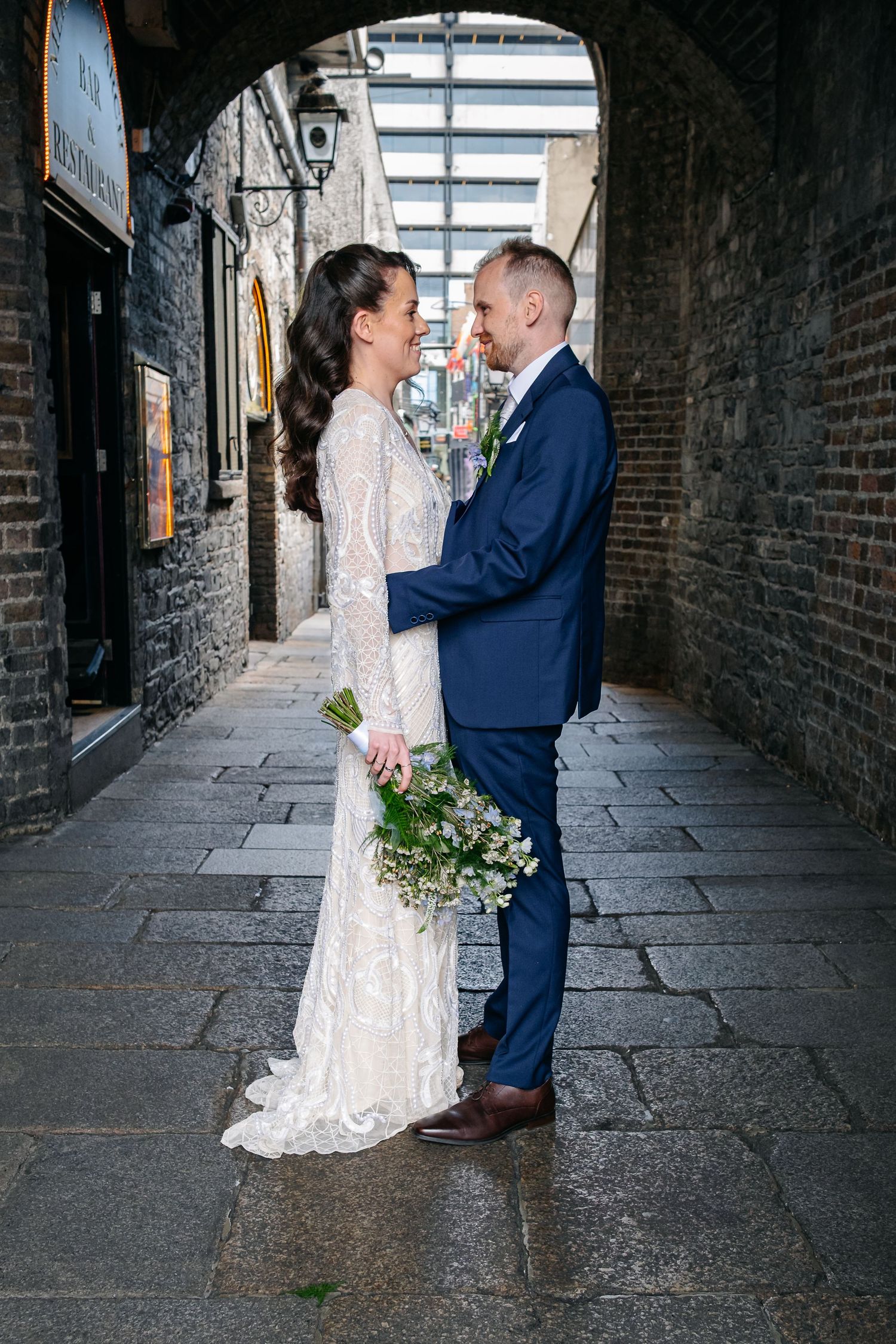 A couple shares an intimate moment in a brick alley with sunlight casting soft shadows on the stone path.