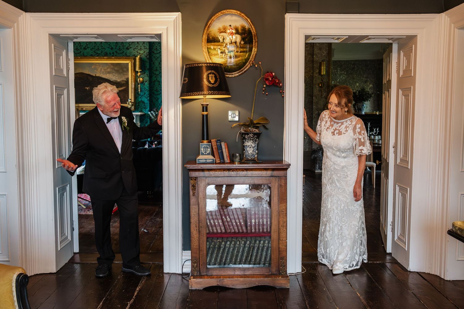 A wedding celebration with a glimpse of people entering through elegant doorways with a decorative gold mirror.