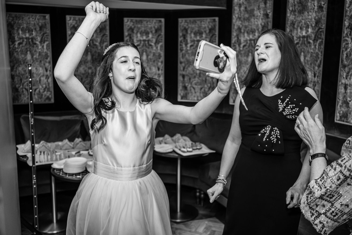 Two women celebrating joyfully with drinks at a wedding reception.