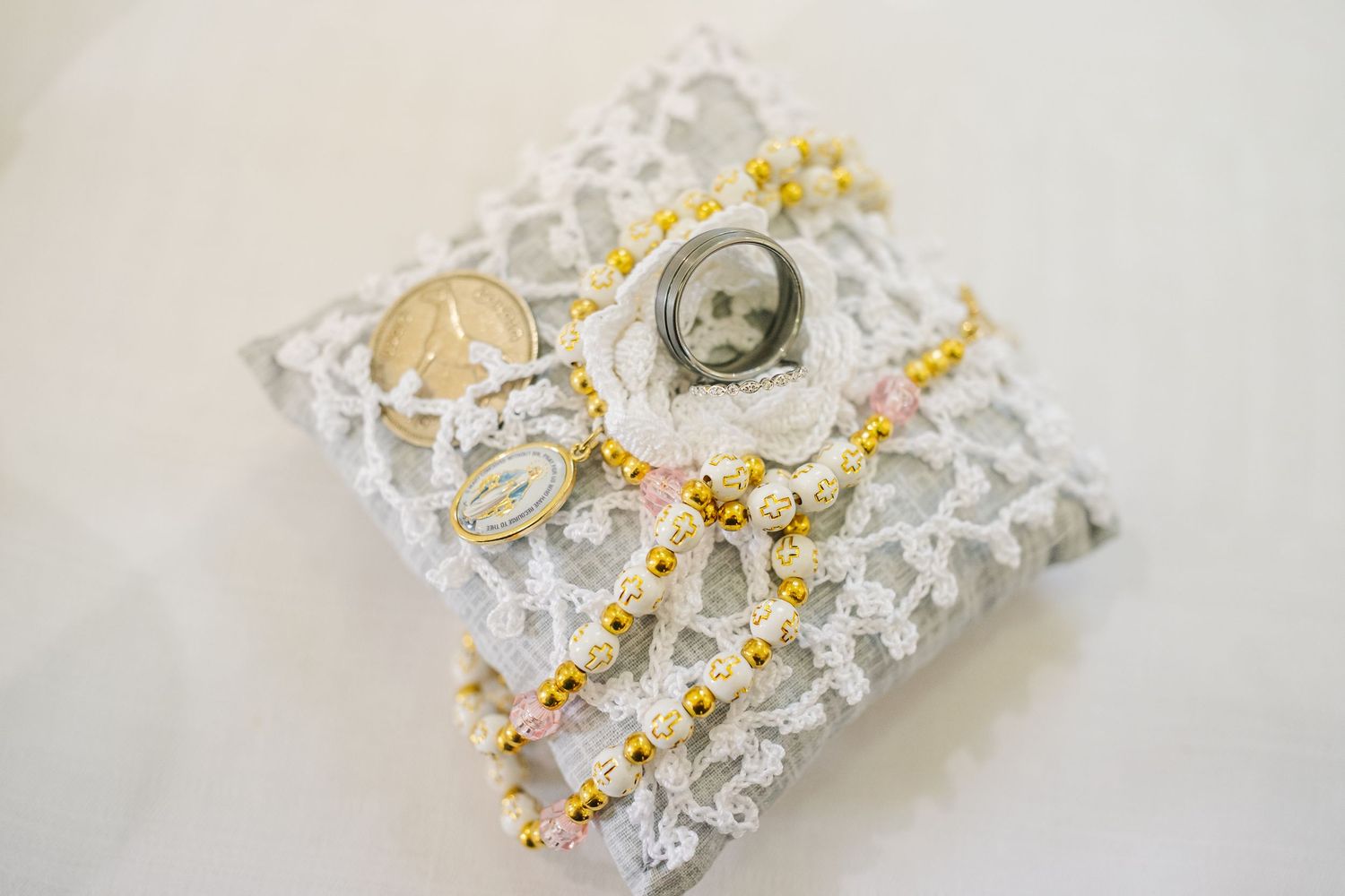 Close-up detail of white crocheted lace trim with delicate yellow flowers and pearls on textured fabric background.