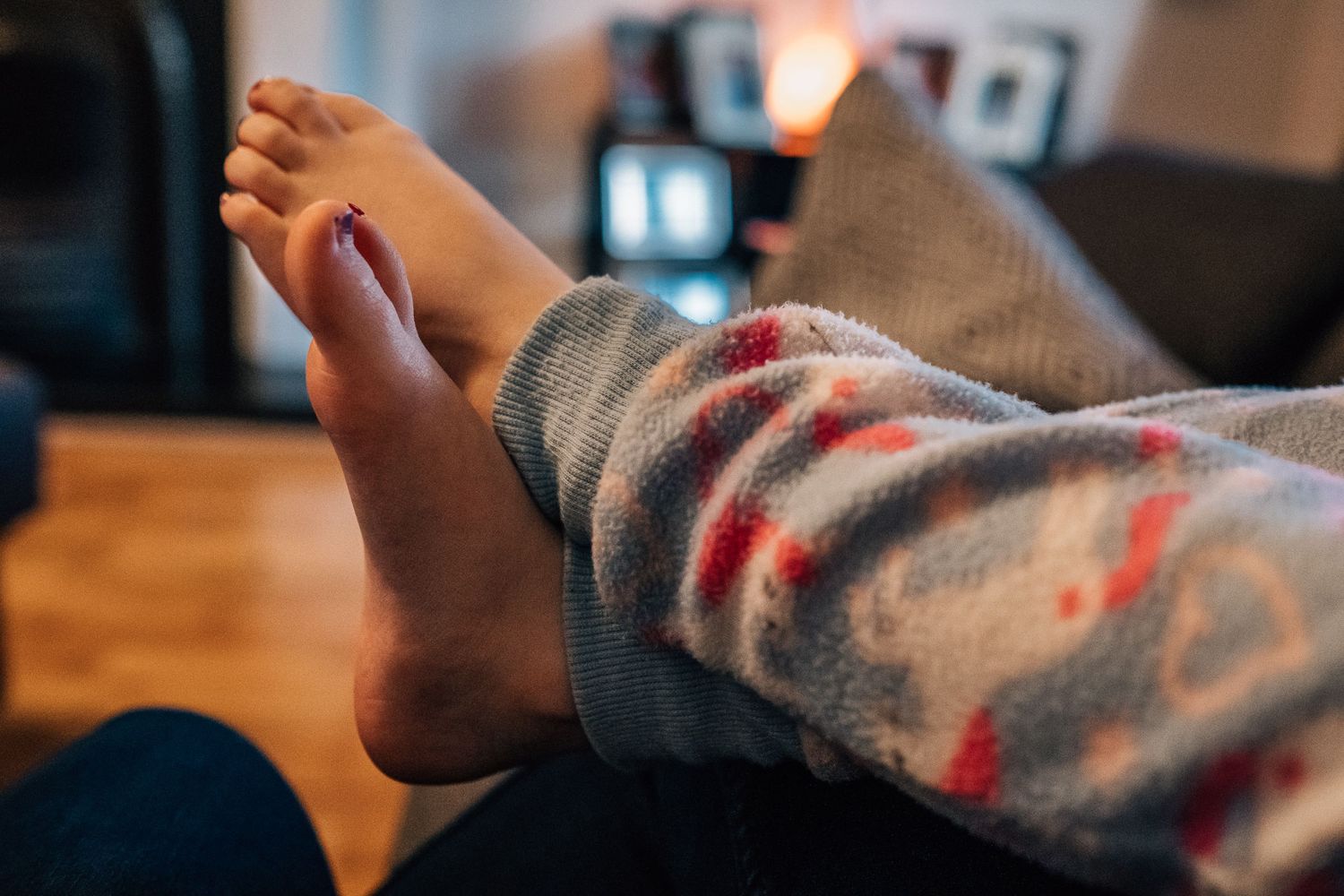 Bare feet in cozy gray and red striped clothing resting on a wooden surface.