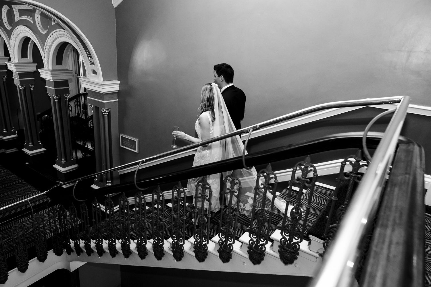 Black and white photo of figures descending an ornate staircase with decorative railings.