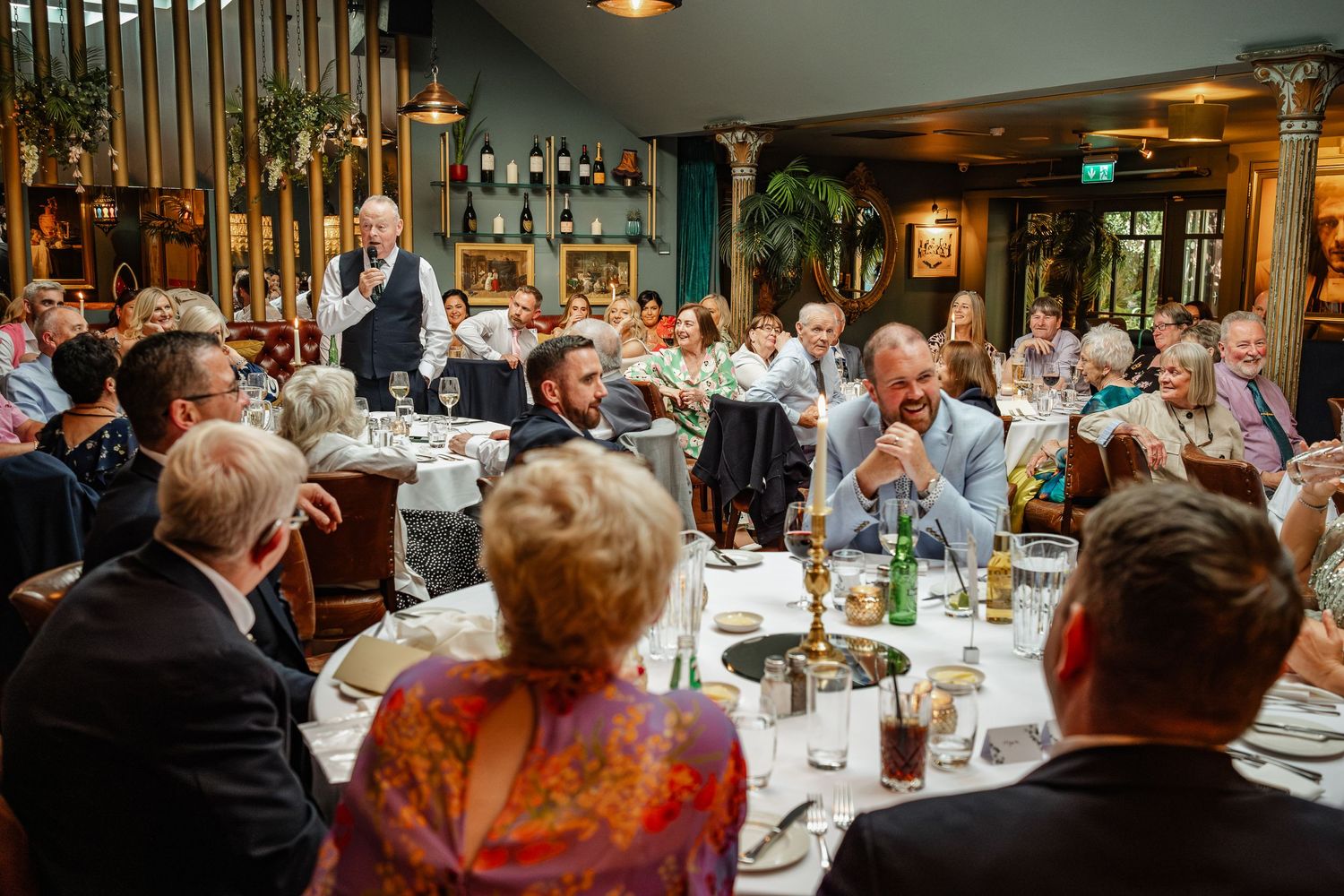 Large wedding reception dinner with guests seated at decorated tables in a rustic venue.