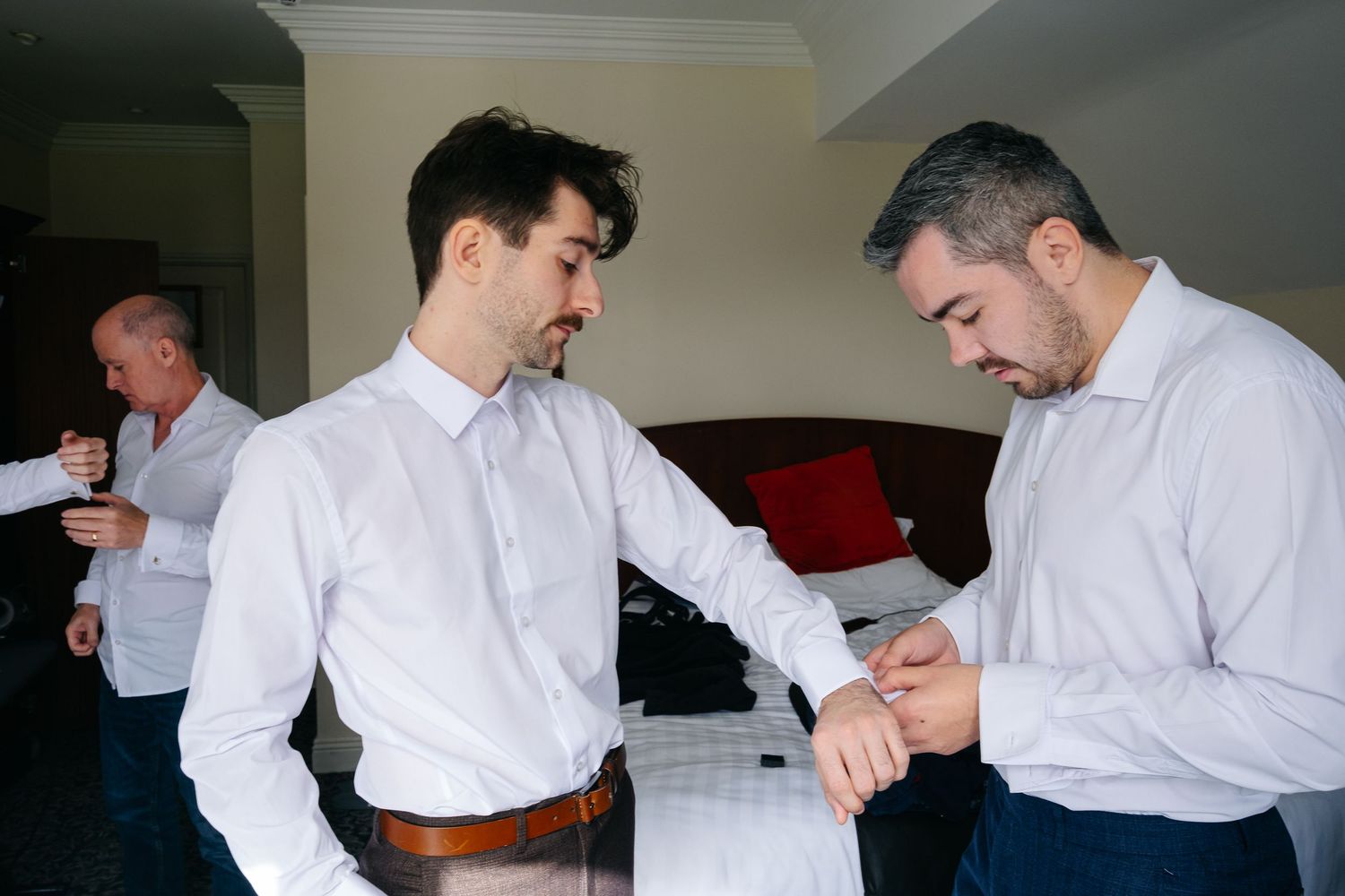 Men in white dress shirts adjusting their formal attire before an event.