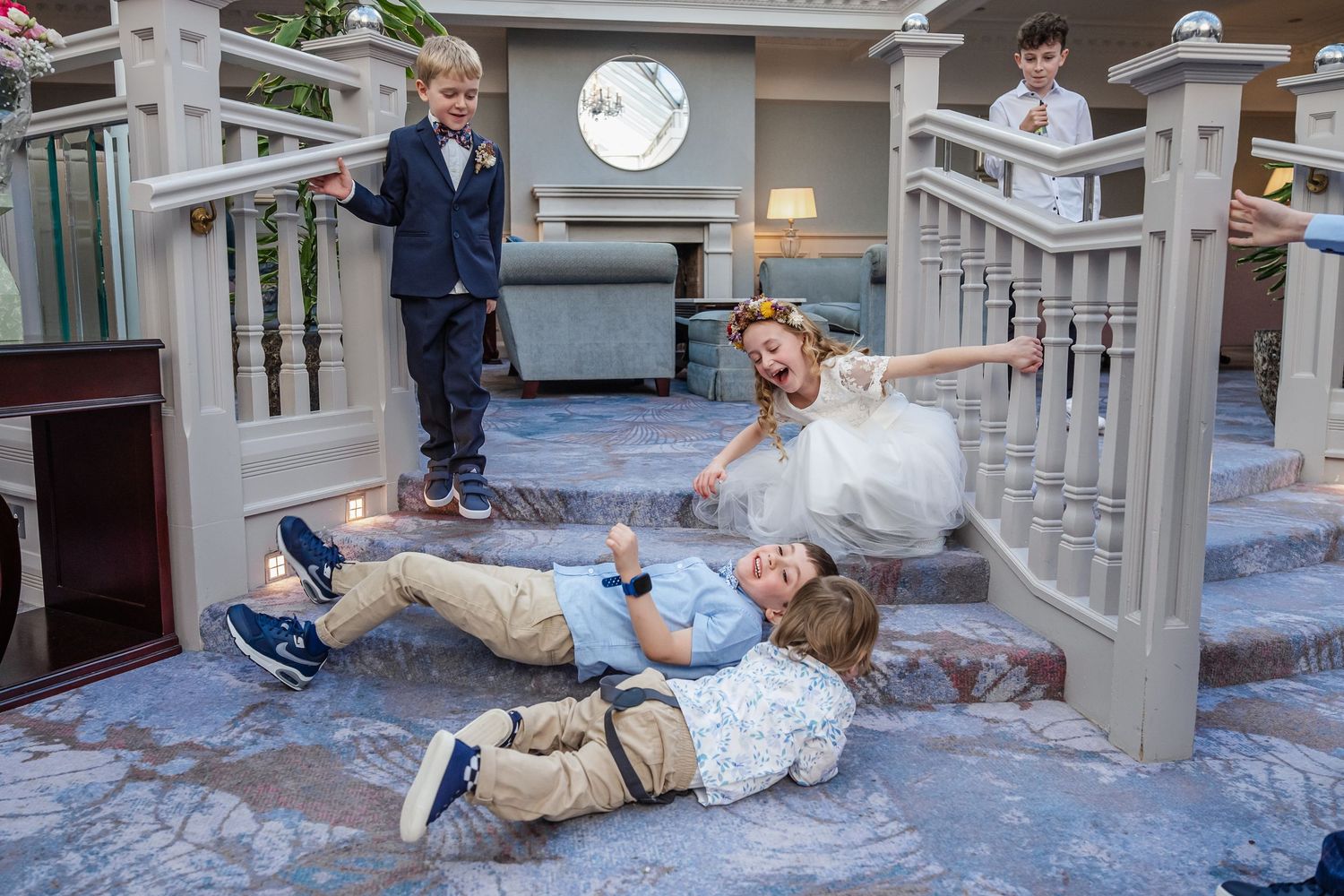 Children playing on elegant staircase at wedding, girl in white dress and boys in formal attire having fun.