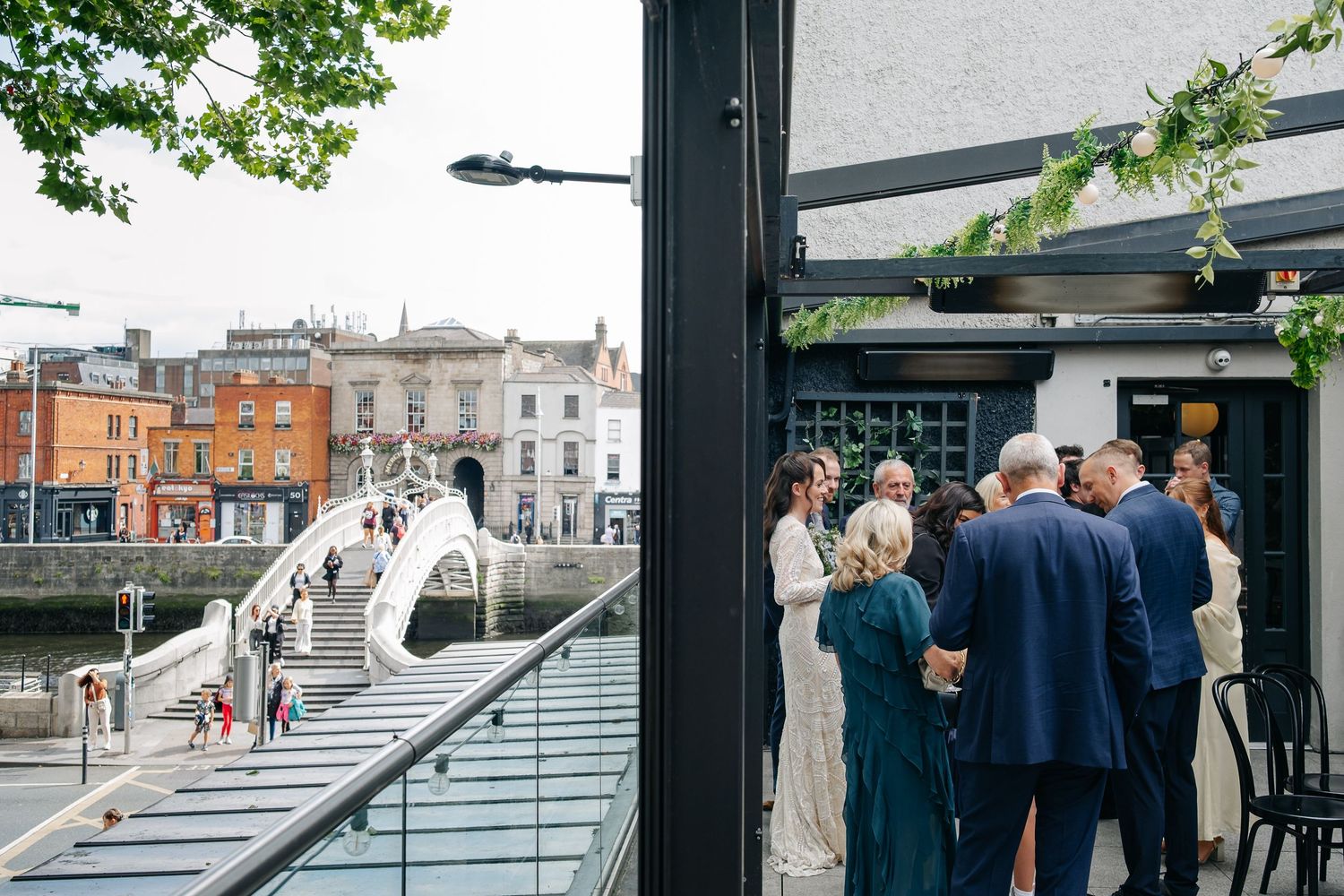 Elegant wedding reception near Ha'penny Bridge, Dublin, with guests mingling on a riverside terrace.
