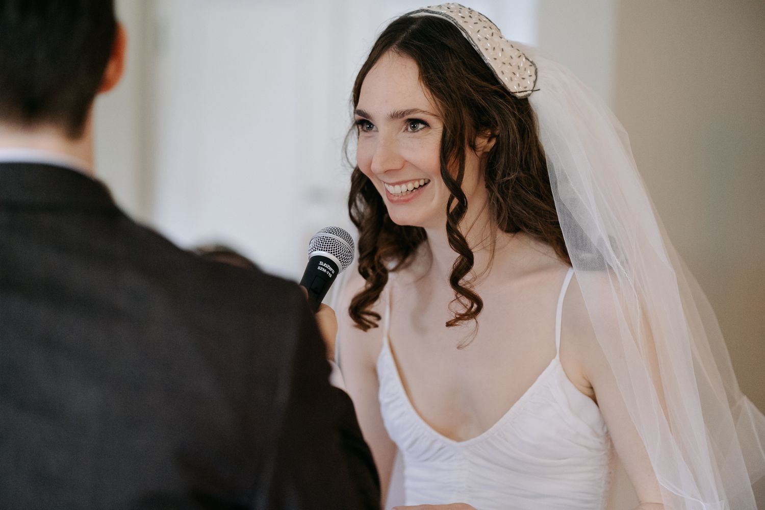 A bride wearing a veil and white dress smiles during wedding ceremony vows.