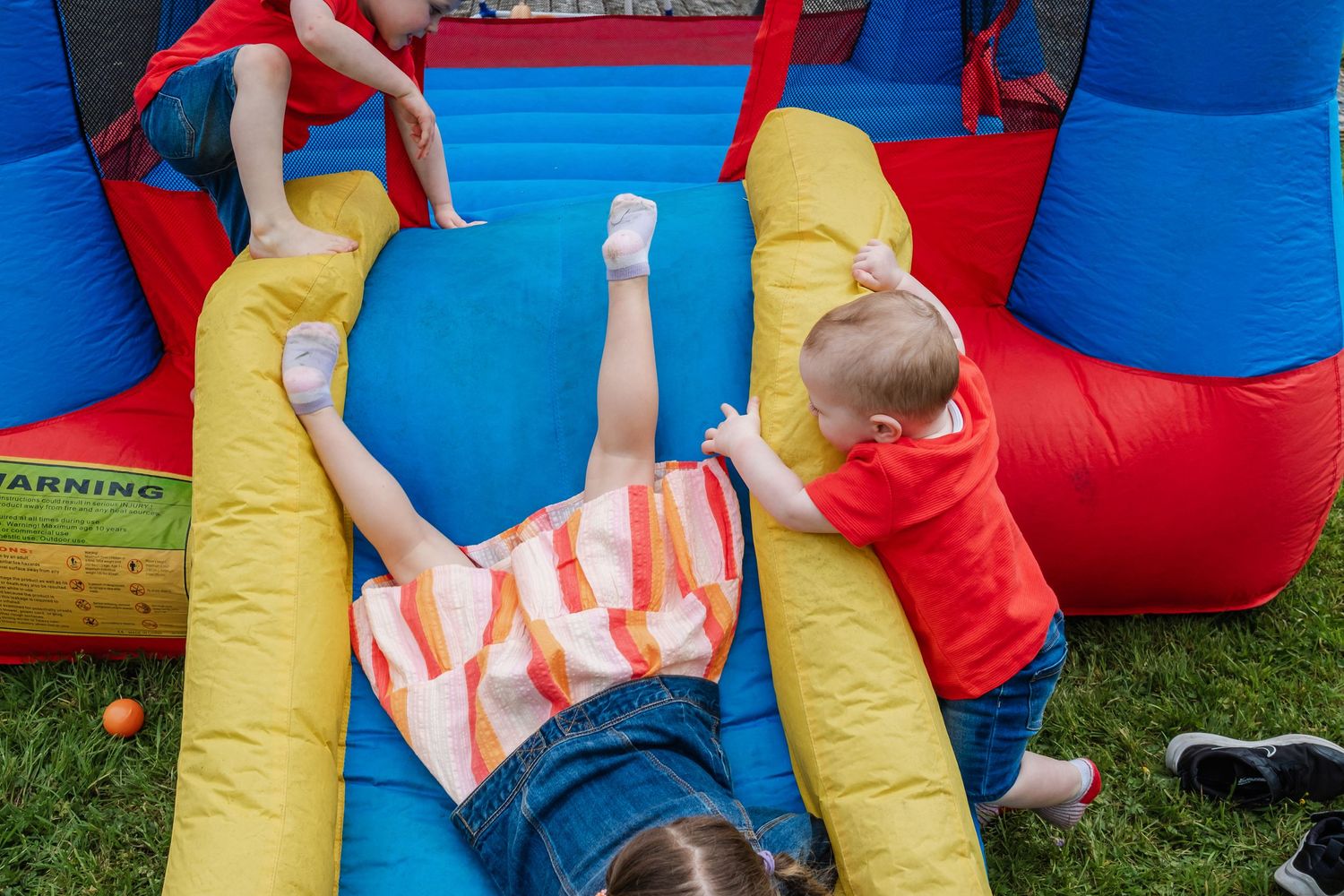 Children playing and sliding on a red and blue inflatable bounce house obstacle course.