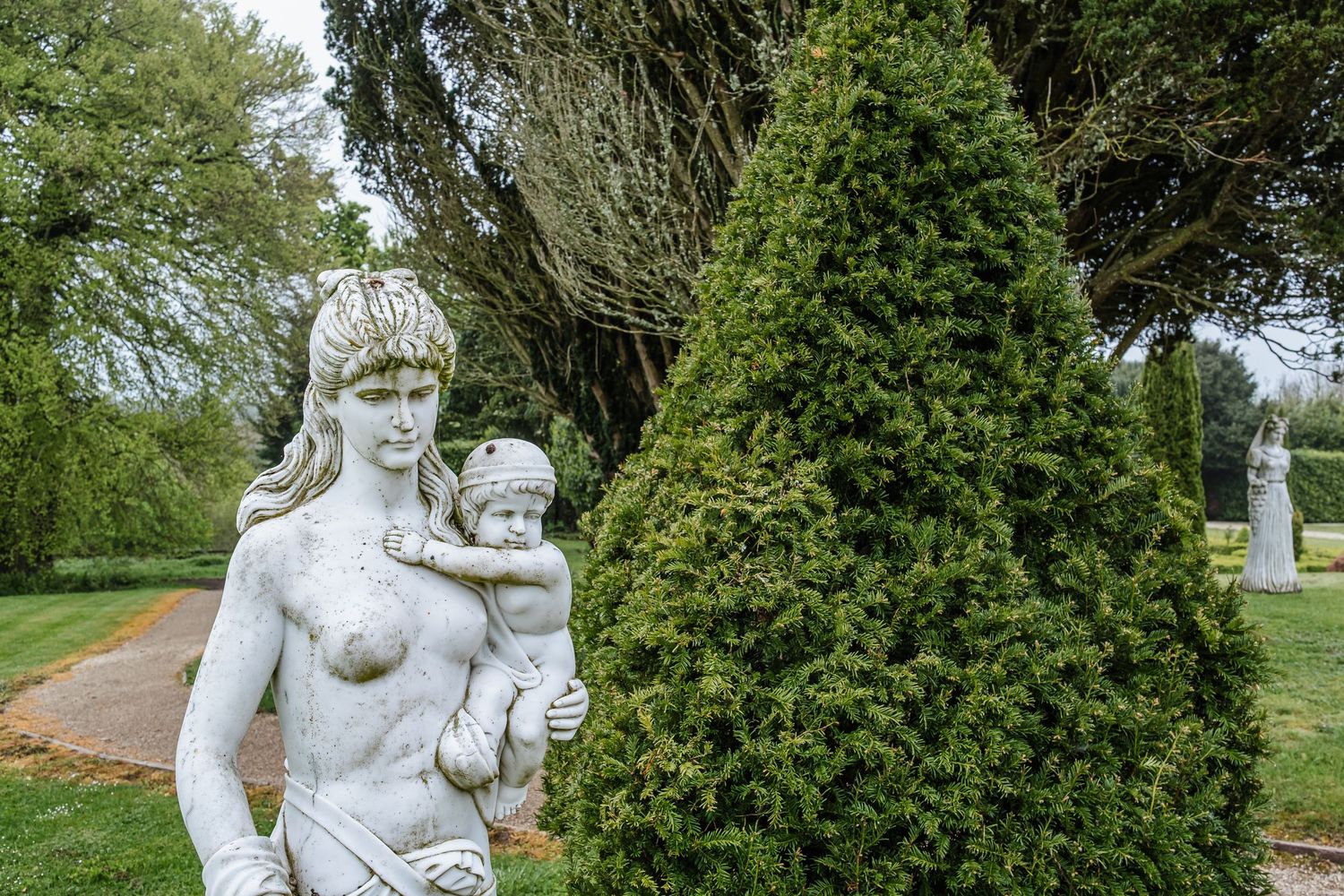 A series of decorative garden statues displayed among green shrubs and trees in an outdoor setting.