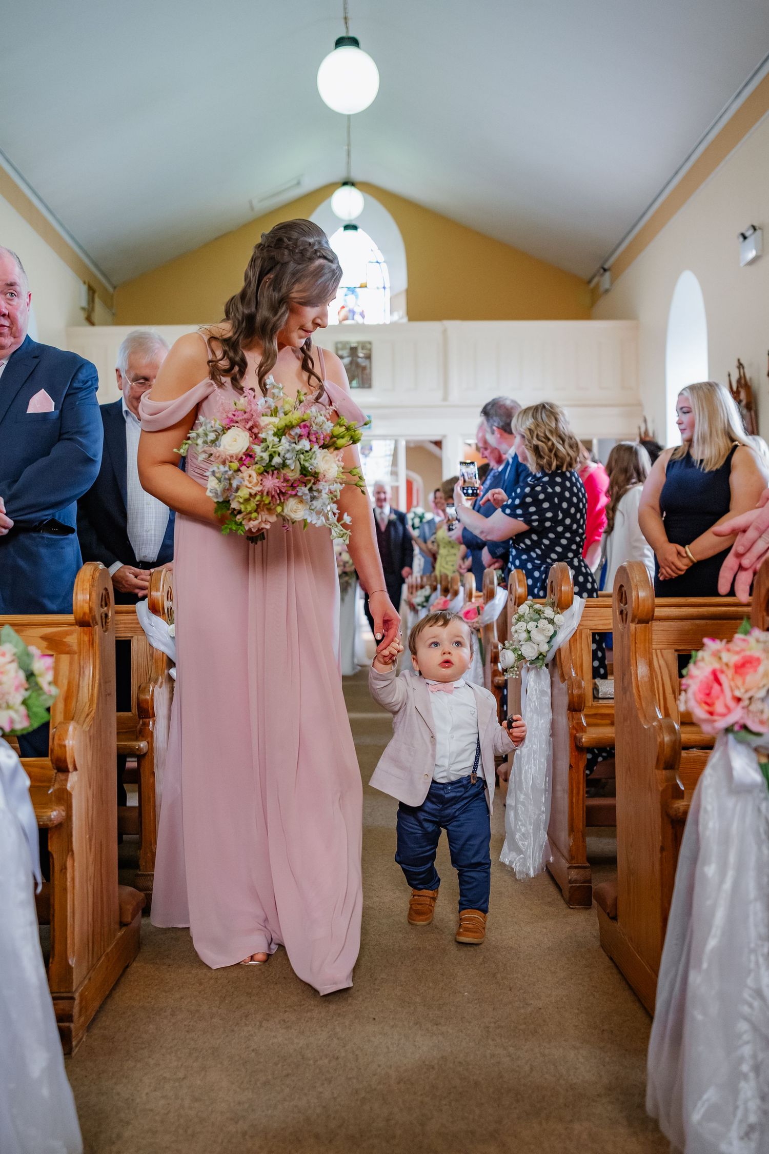 Wedding party members standing in the church aisles with pink bridesmaid dresses and floral bouquets.