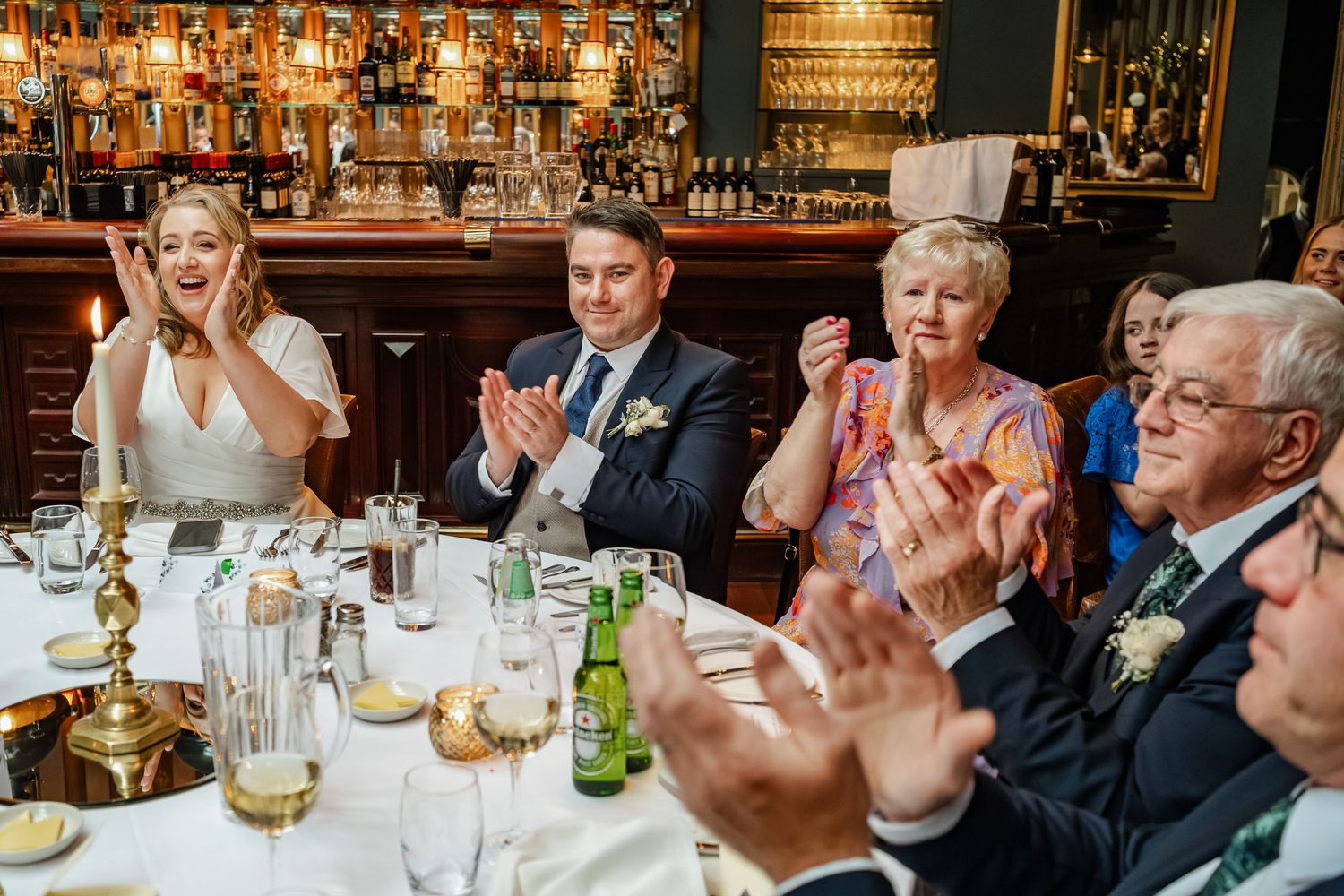 Wedding guests applauding during speeches at an elegant bar reception.