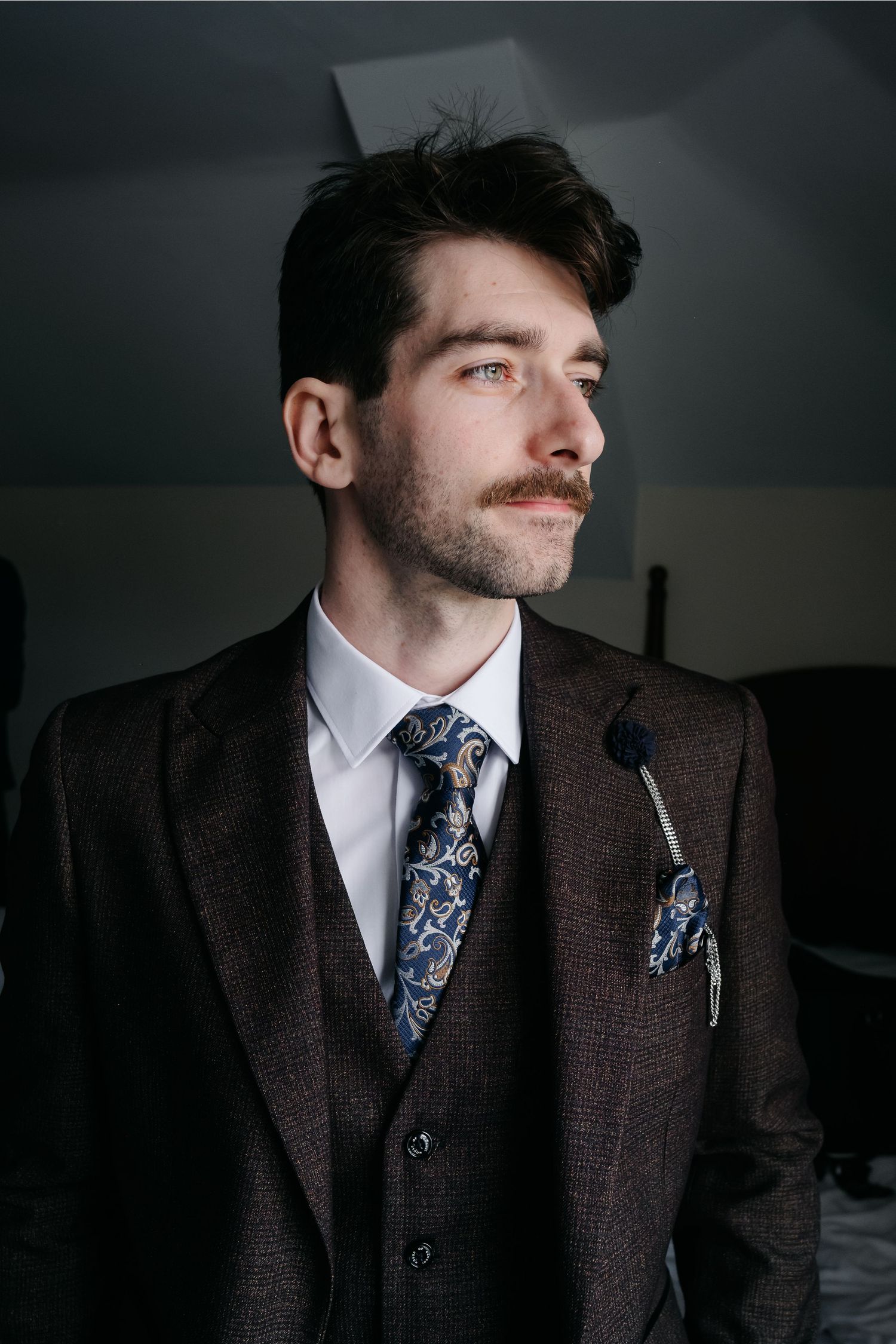 Dramatic portraits of someone in a dark tweed suit with floral tie against moody lighting.
