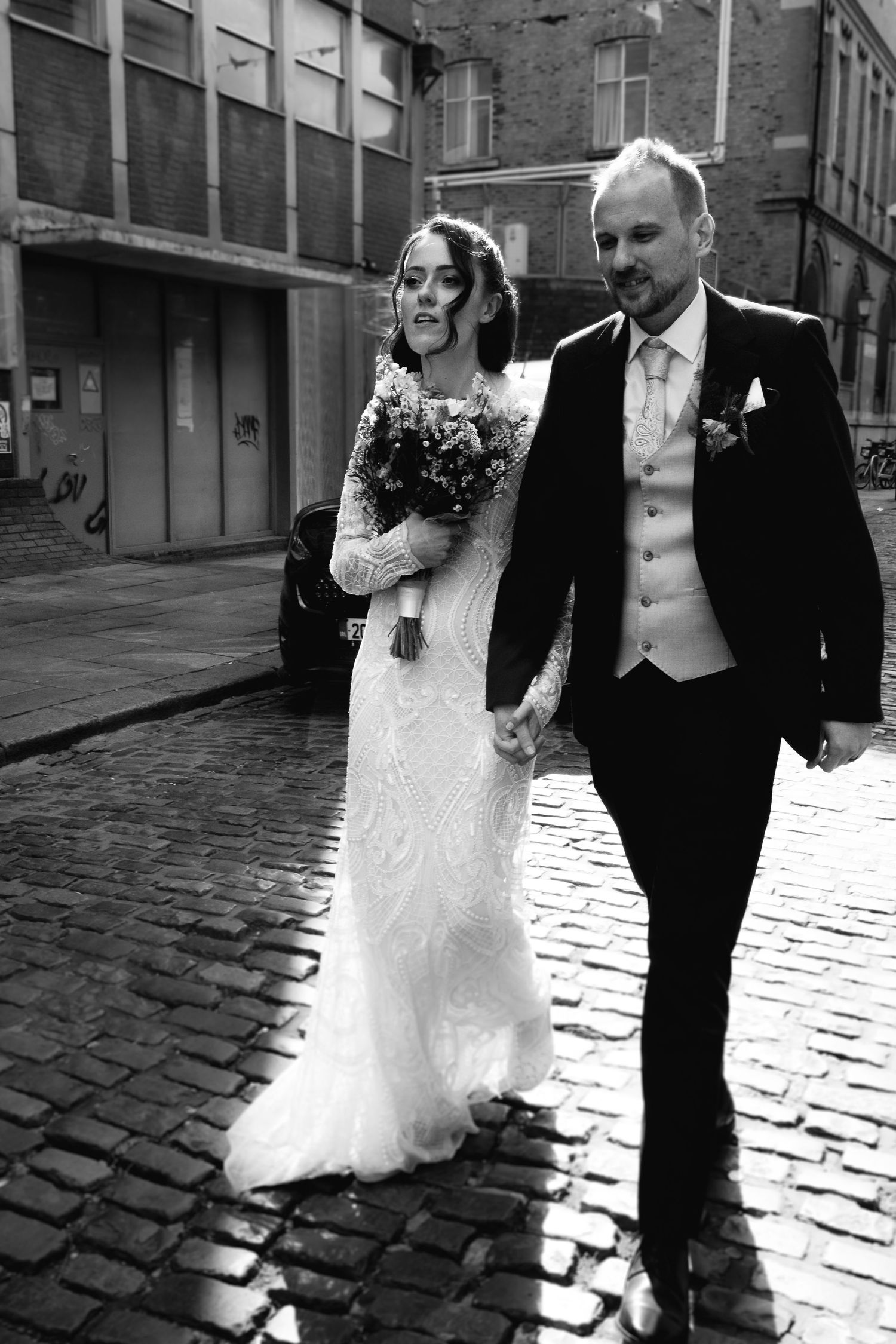 A black and white photo series of a bride and groom walking together on a cobblestone street on their wedding day.
