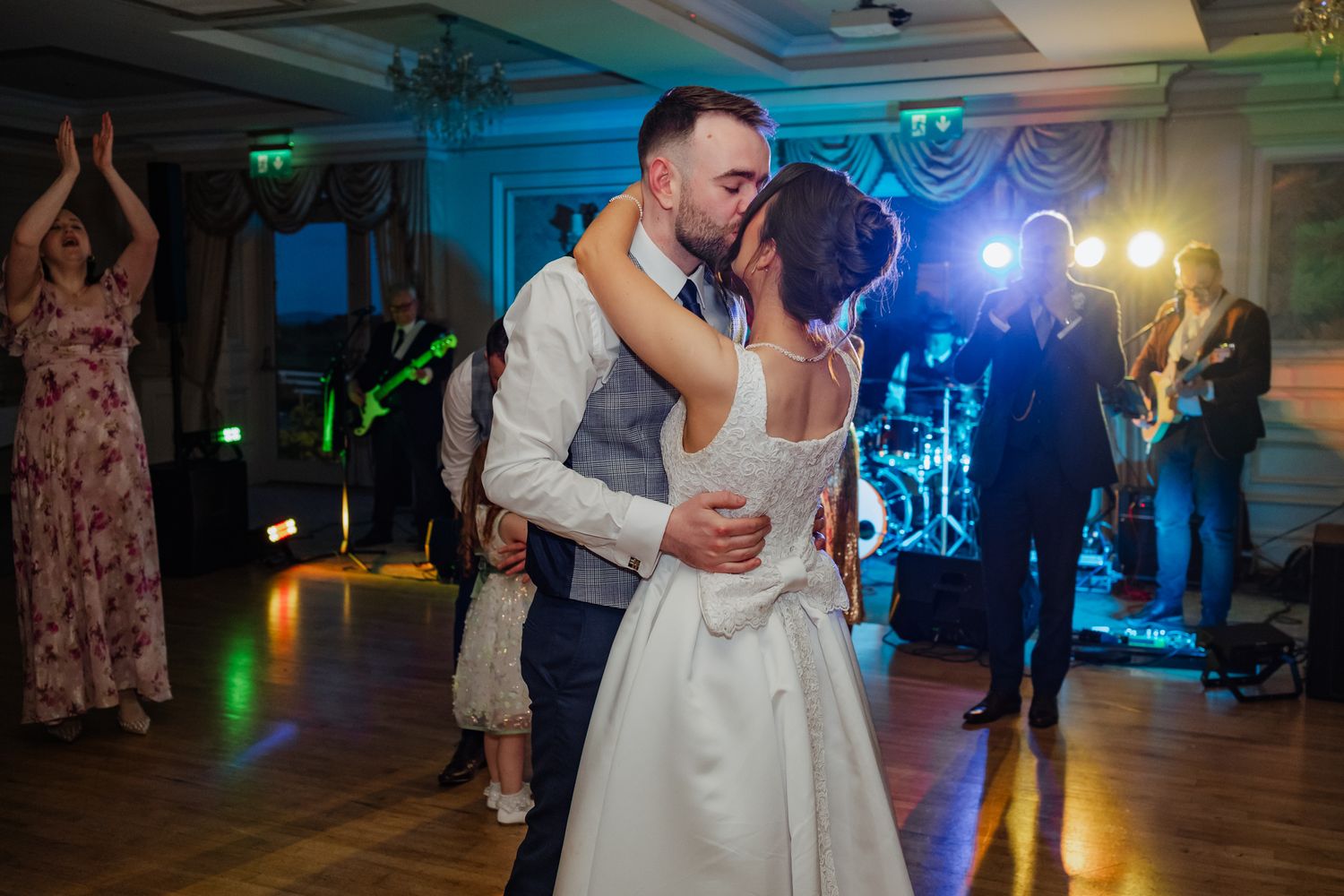 Bride and groom share their first dance kiss at wedding reception with live band performing in background.