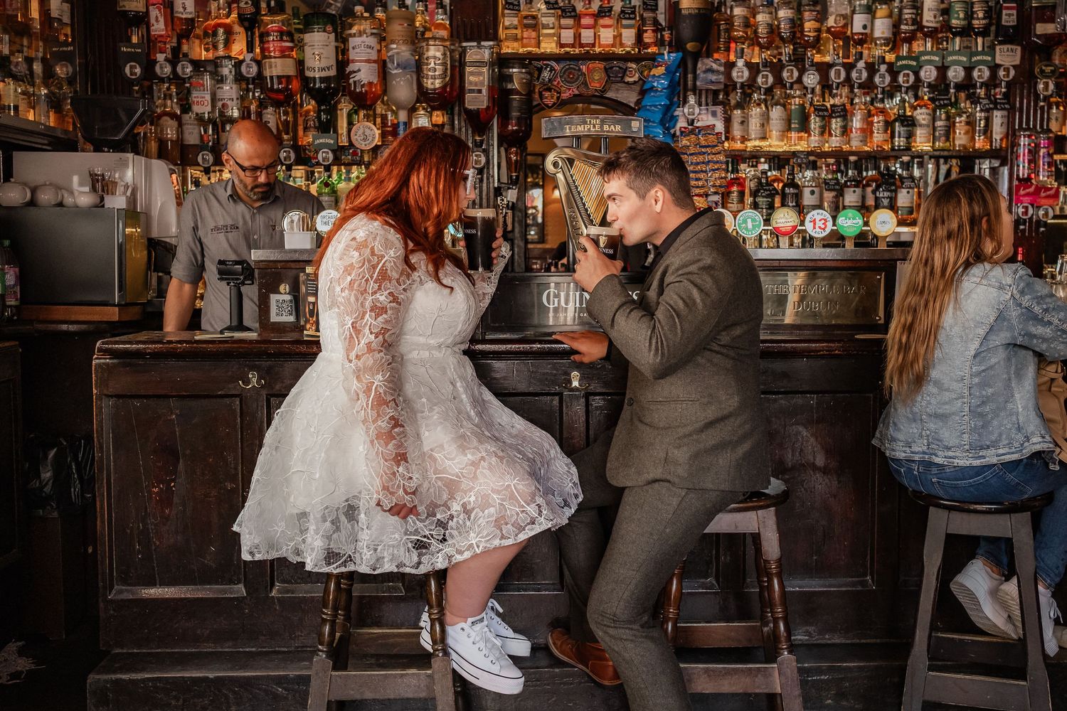 Wedding celebration continues at rustic bar with wooden details and vintage bottle display.