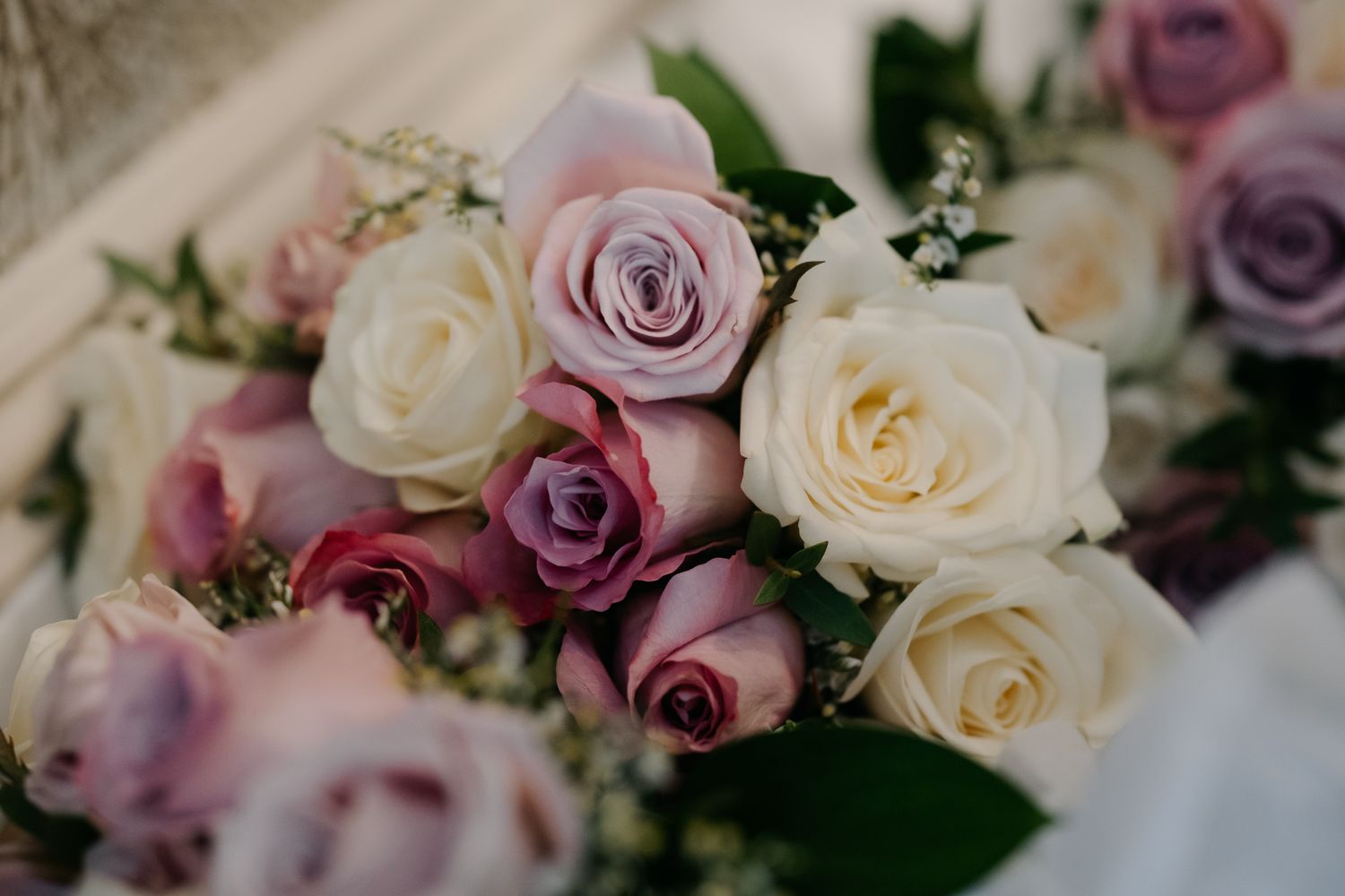 Close-up of a elegant bridal bouquet featuring white, pink, and lavender roses with delicate greenery.
