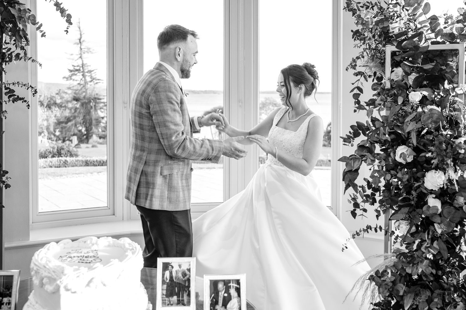 Black and white photo of a bride and groom exchanging rings at their wedding ceremony indoors.
