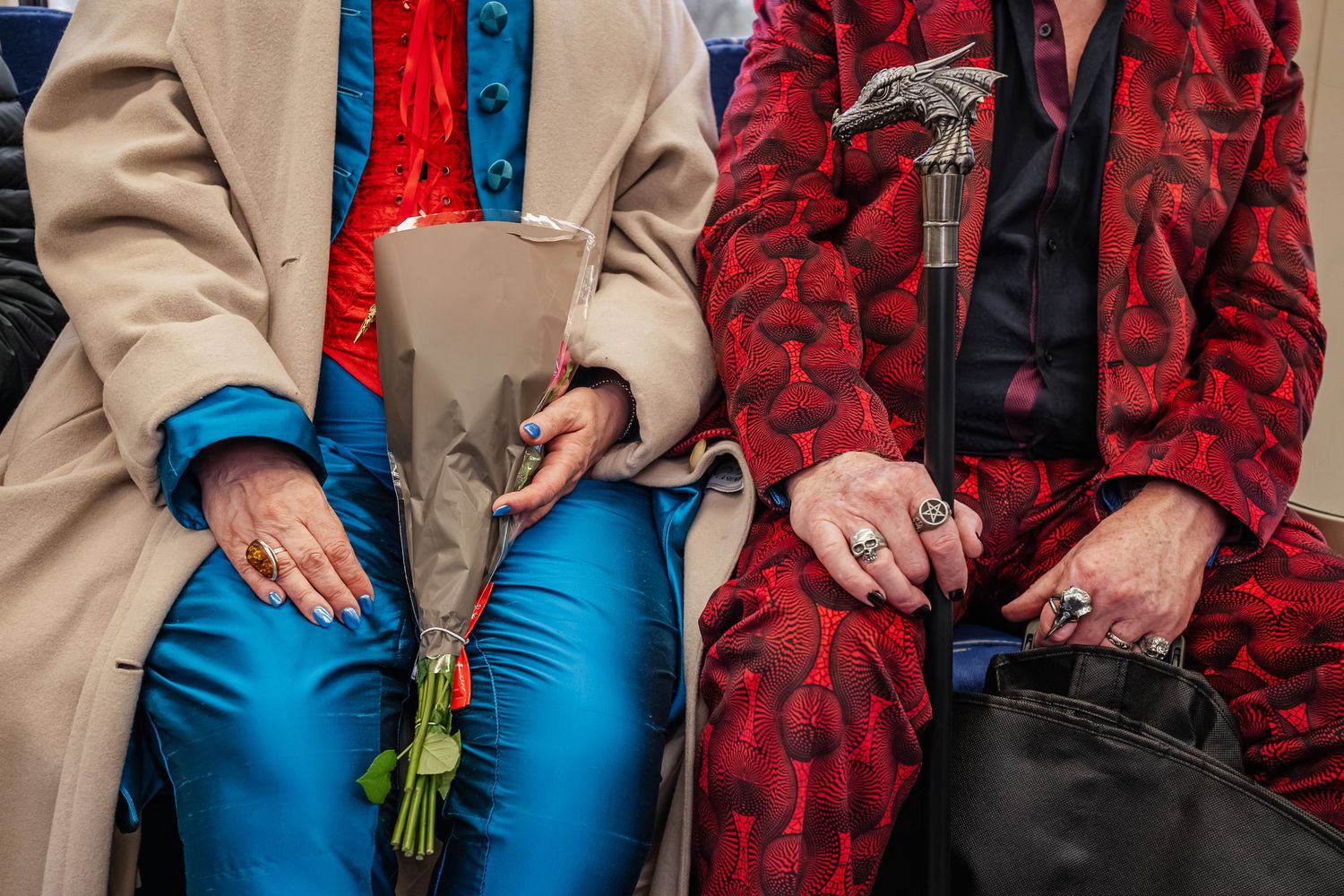 Close-up of two people sitting together wearing contrasting outfits in beige and red.