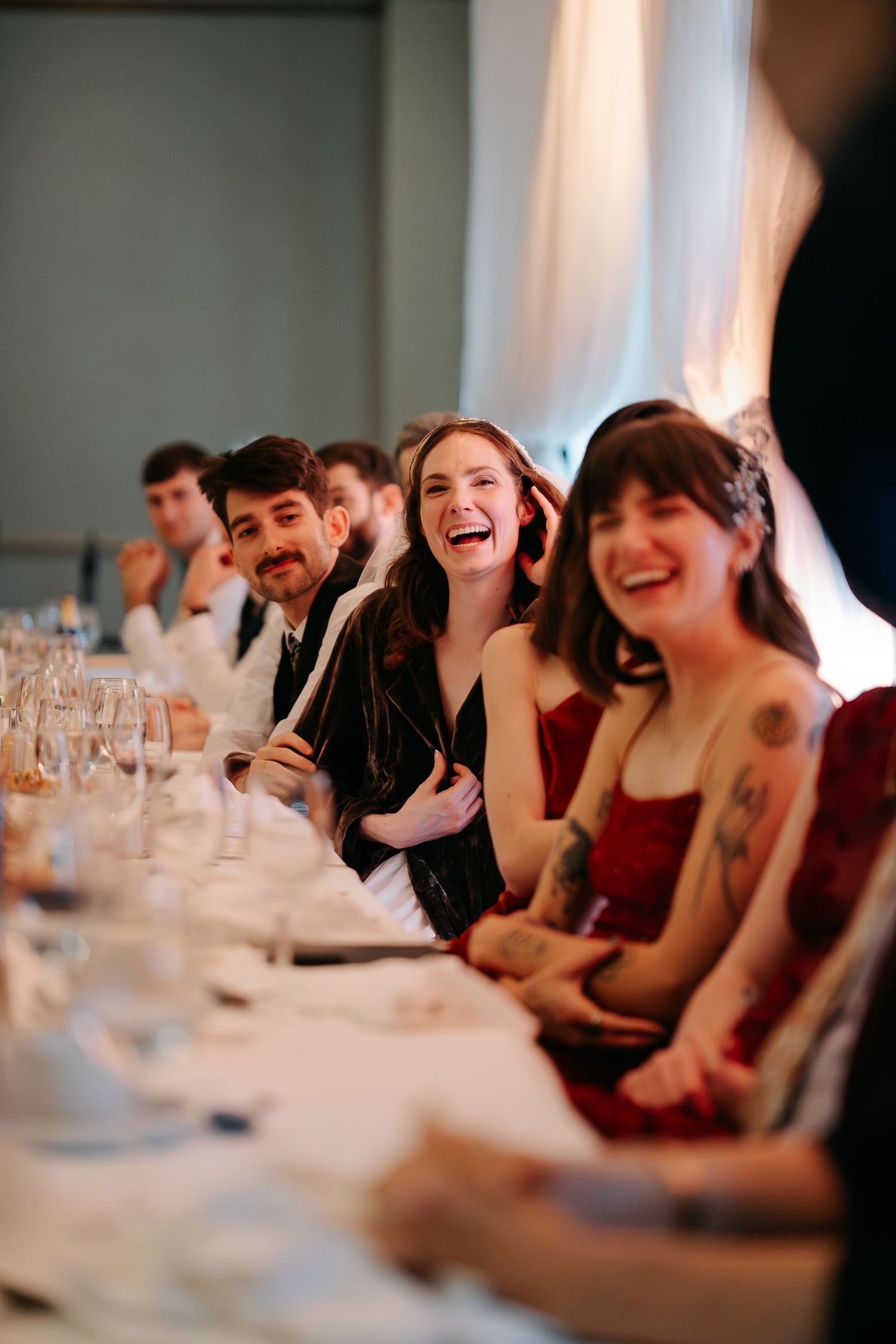 Wedding reception guests enjoying candid moments at a banquet table with soft lighting.