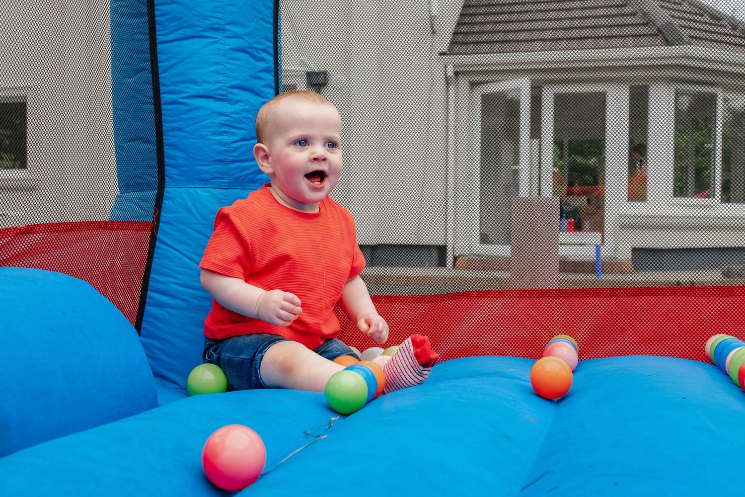 Excited child playing with colorful balls on a blue and red inflatable bounce house.