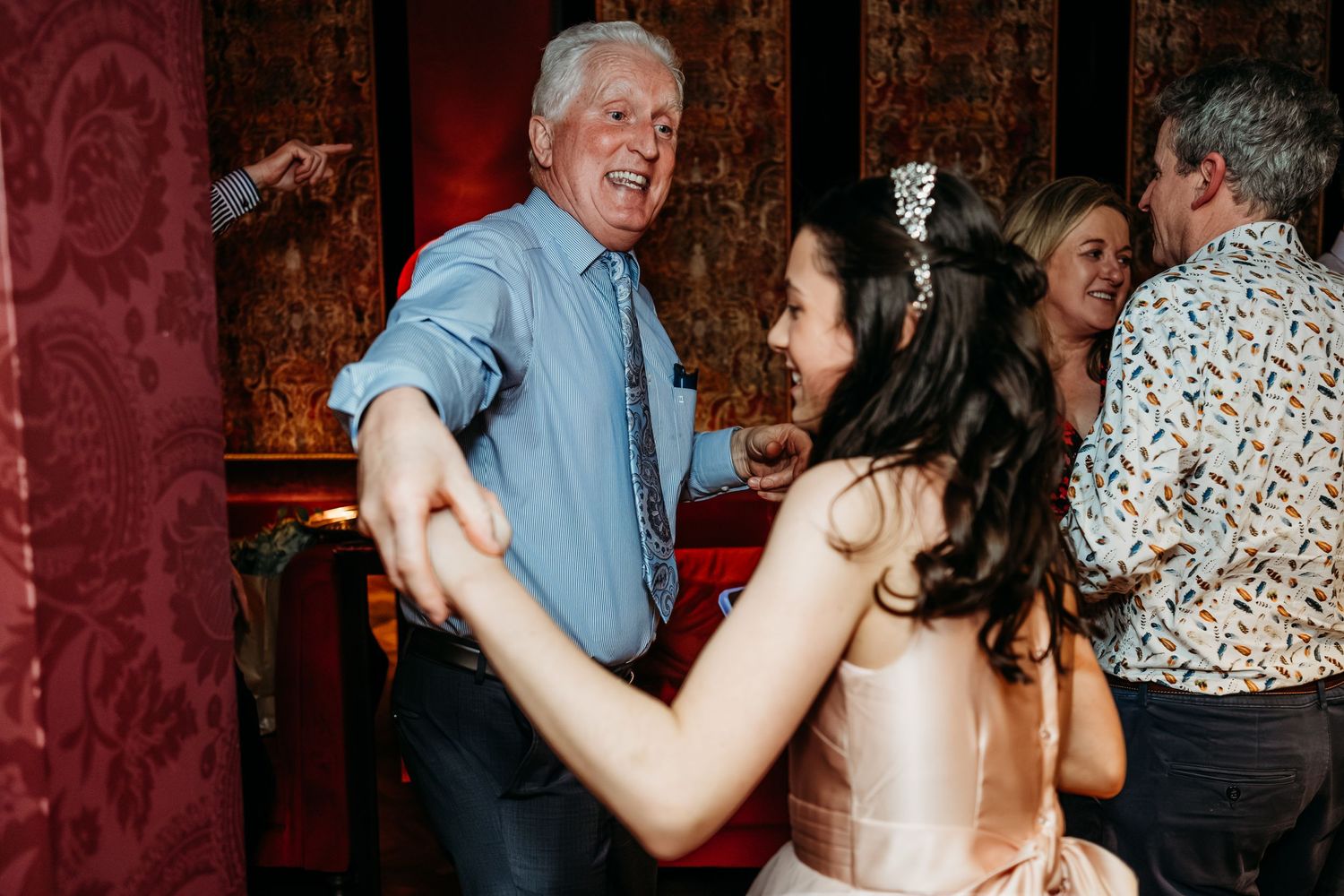 A couple shares a lively dance together at an elegant venue with red damask wallpaper.