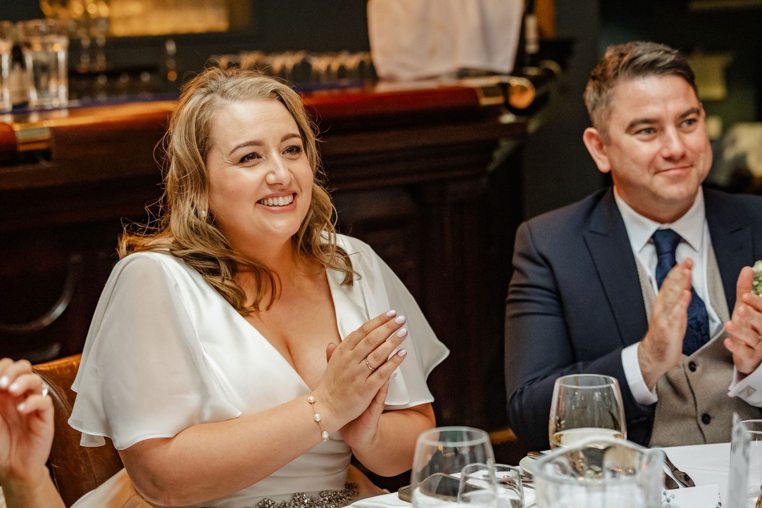 Wedding guests applaud during a reception dinner at an elegant restaurant bar setting.