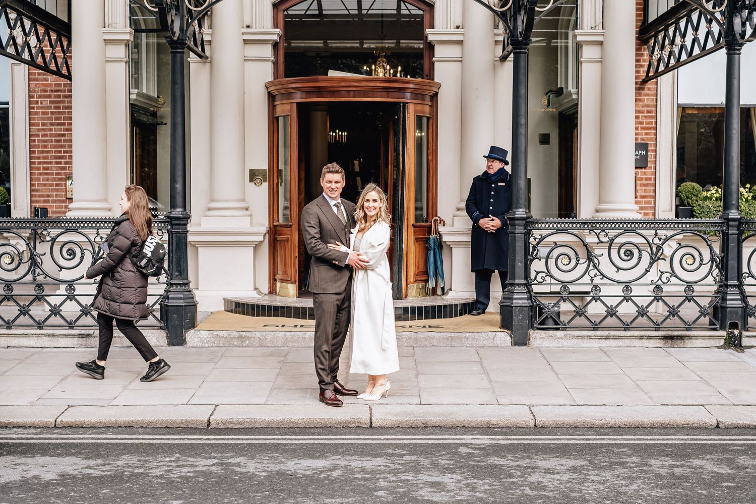 Winter wedding scene at the entrance of a historic building with ornate ironwork.